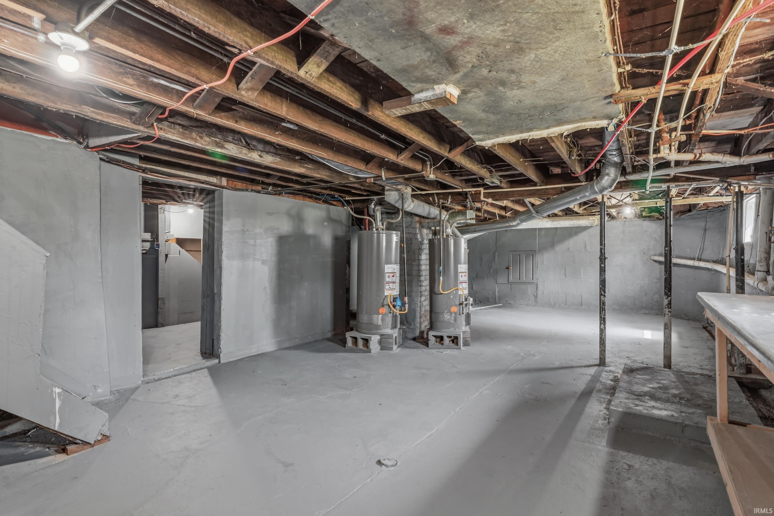 Spacious basement featuring painted concrete flooring, exposed ceiling joists, two water heaters, and structural support beams