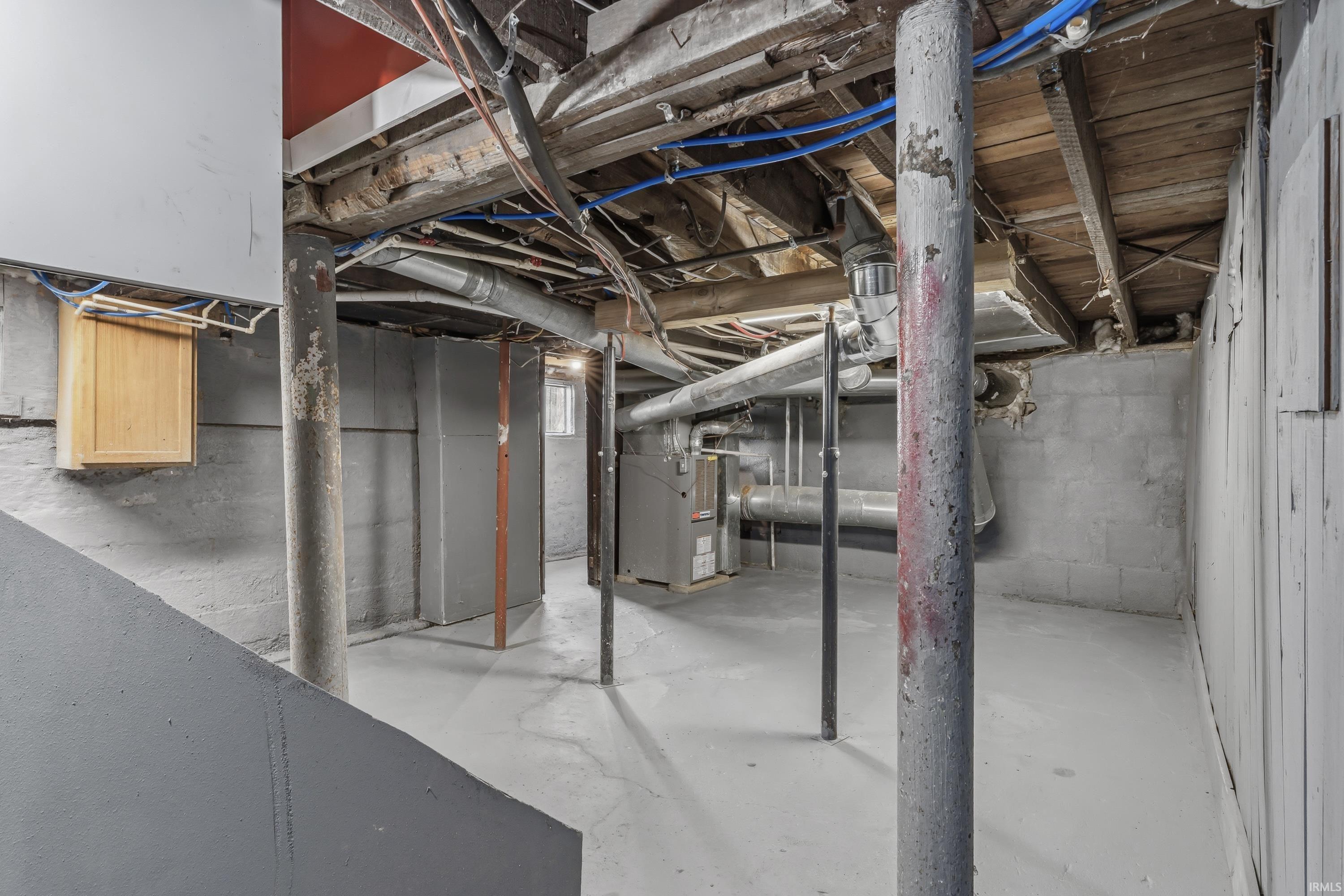 Basement space featuring concrete flooring, exposed ceiling joists, and visible utility lines