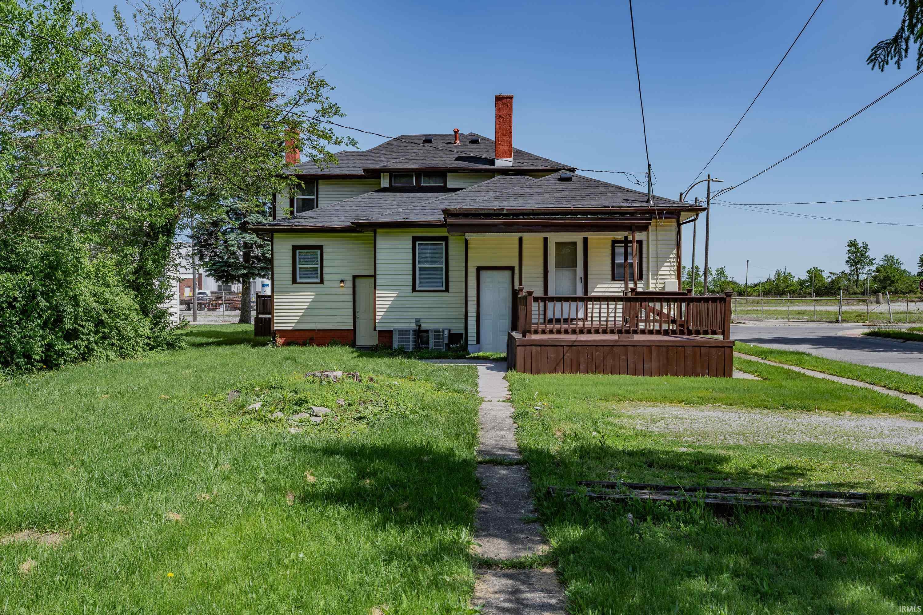Rear exterior featuring a spacious wood-finish deck, light-colored siding, dark trim windows, and two prominent chimneys
