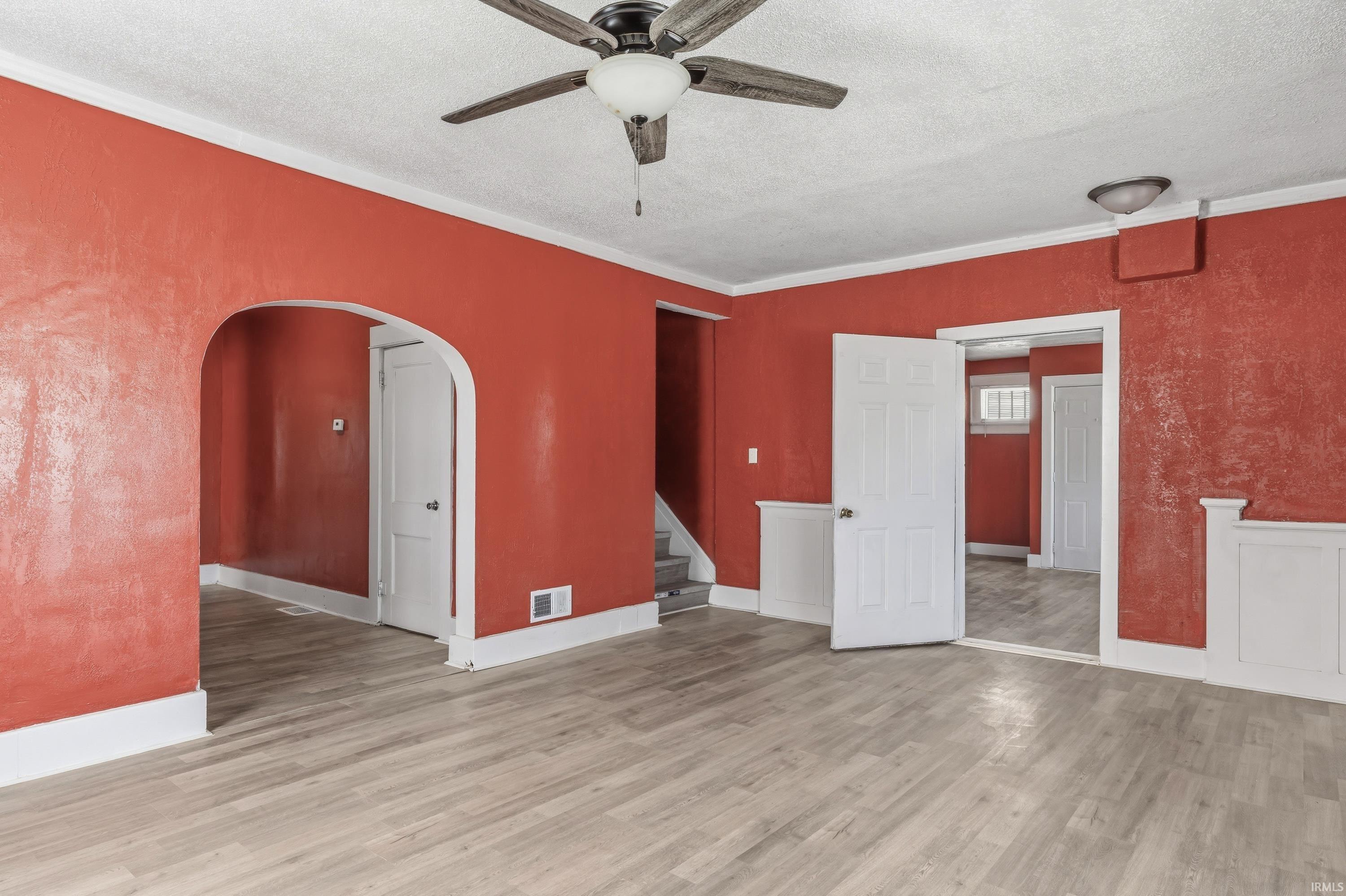 Spacious interior room featuring light wood-finish flooring, white crown molding, and wainscoting