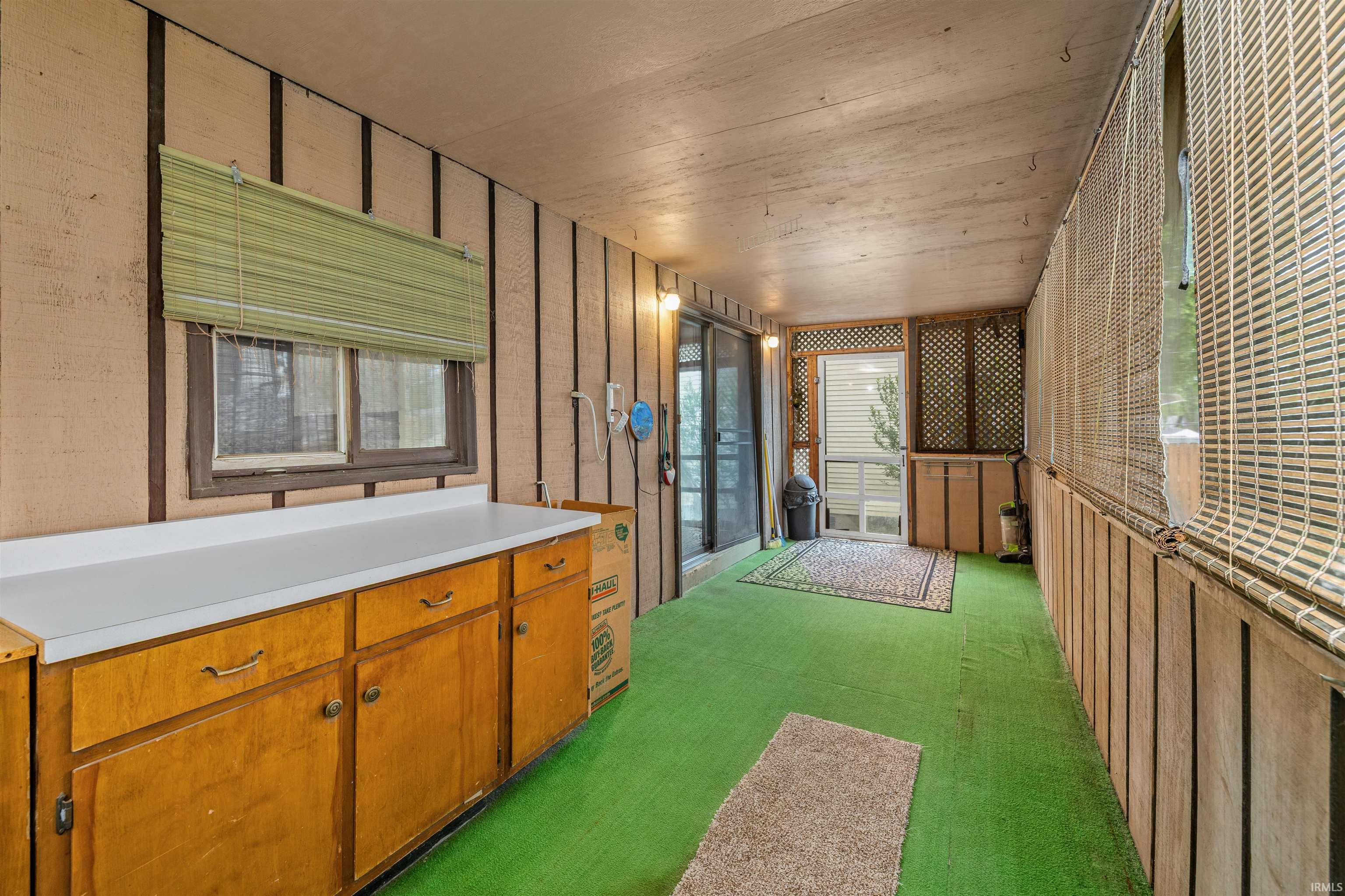 Enclosed sunroom featuring a green floor covering, wood paneling, built-in cabinetry with a white countertop, and sliding glass doors