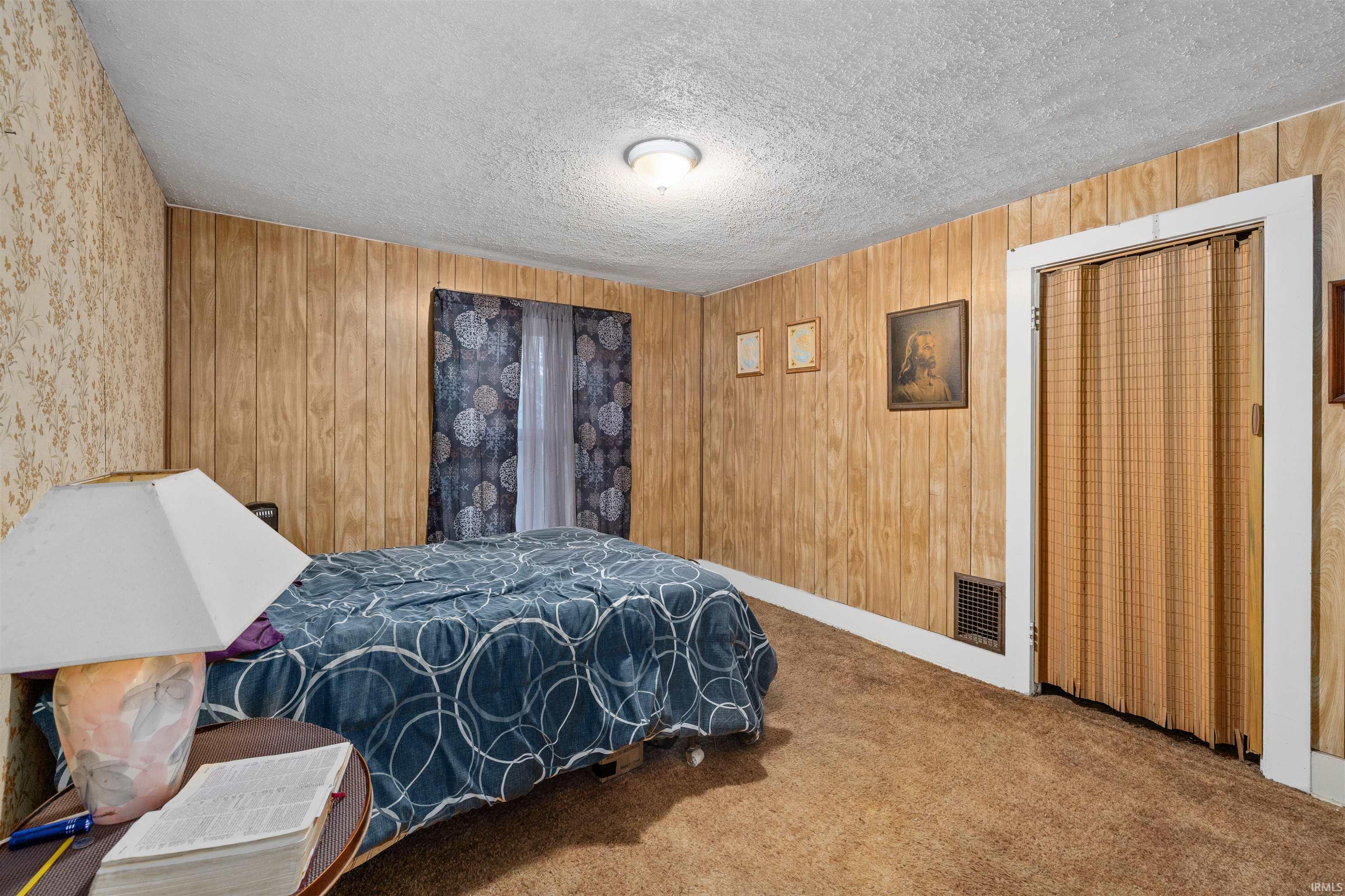 Carpeted room featuring wood-finish paneling, a textured ceiling, and a folding accordion door