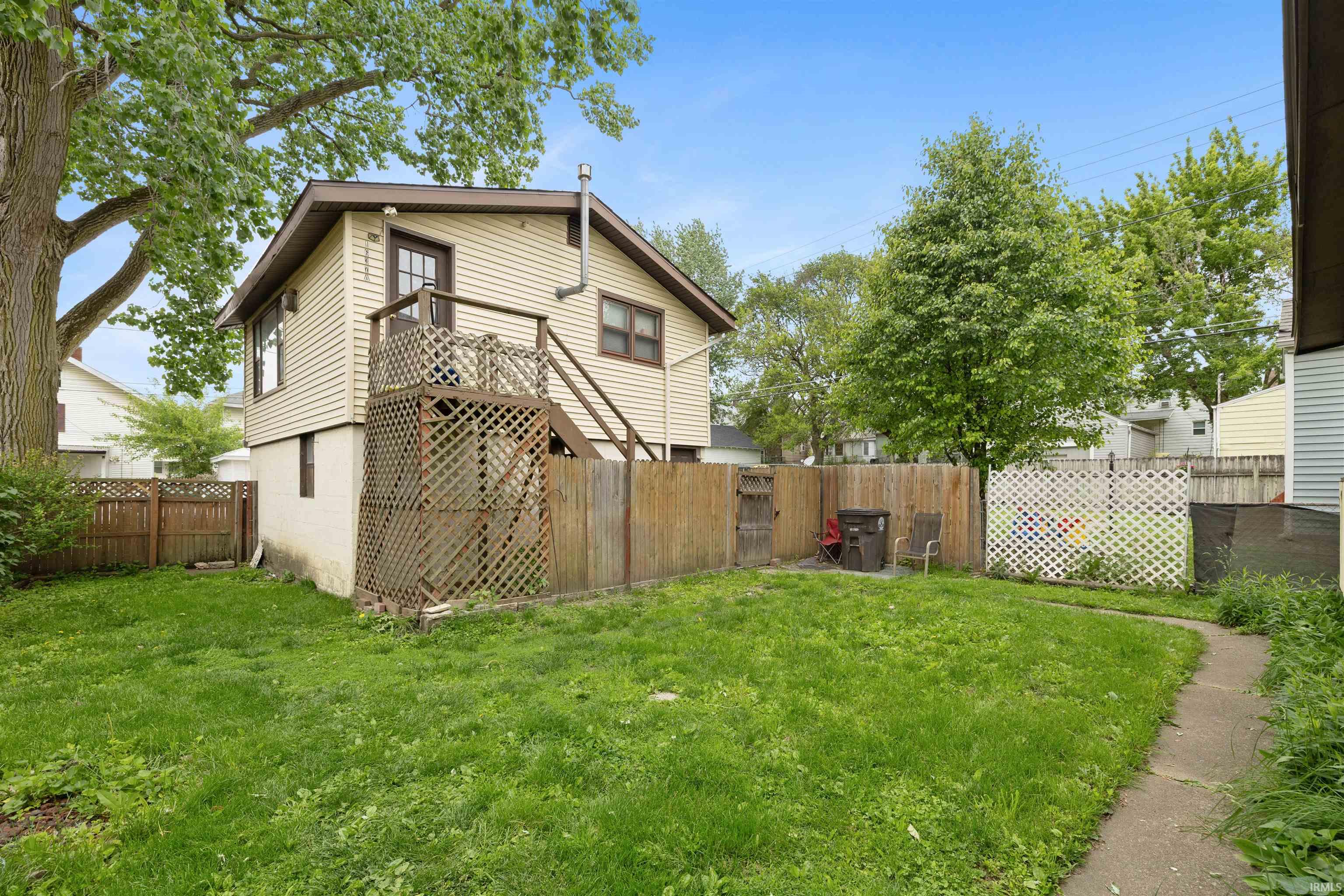 Rear exterior with a second-story deck and stairs, featuring neutral siding and a wood privacy fence