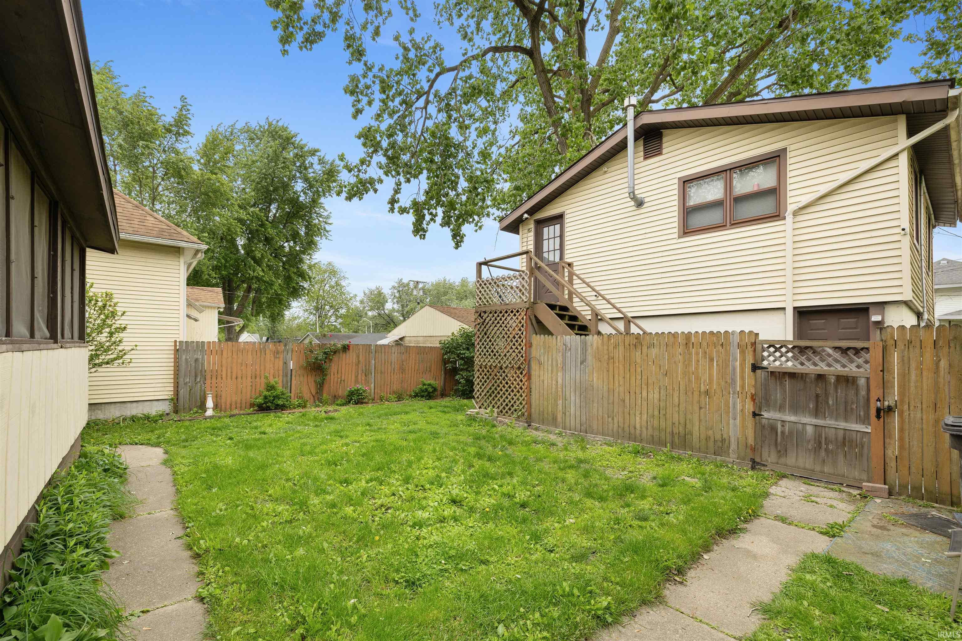 Fenced backyard with established lawn, concrete pathway, and a rear building with exterior stairs and an upper-level entry door
