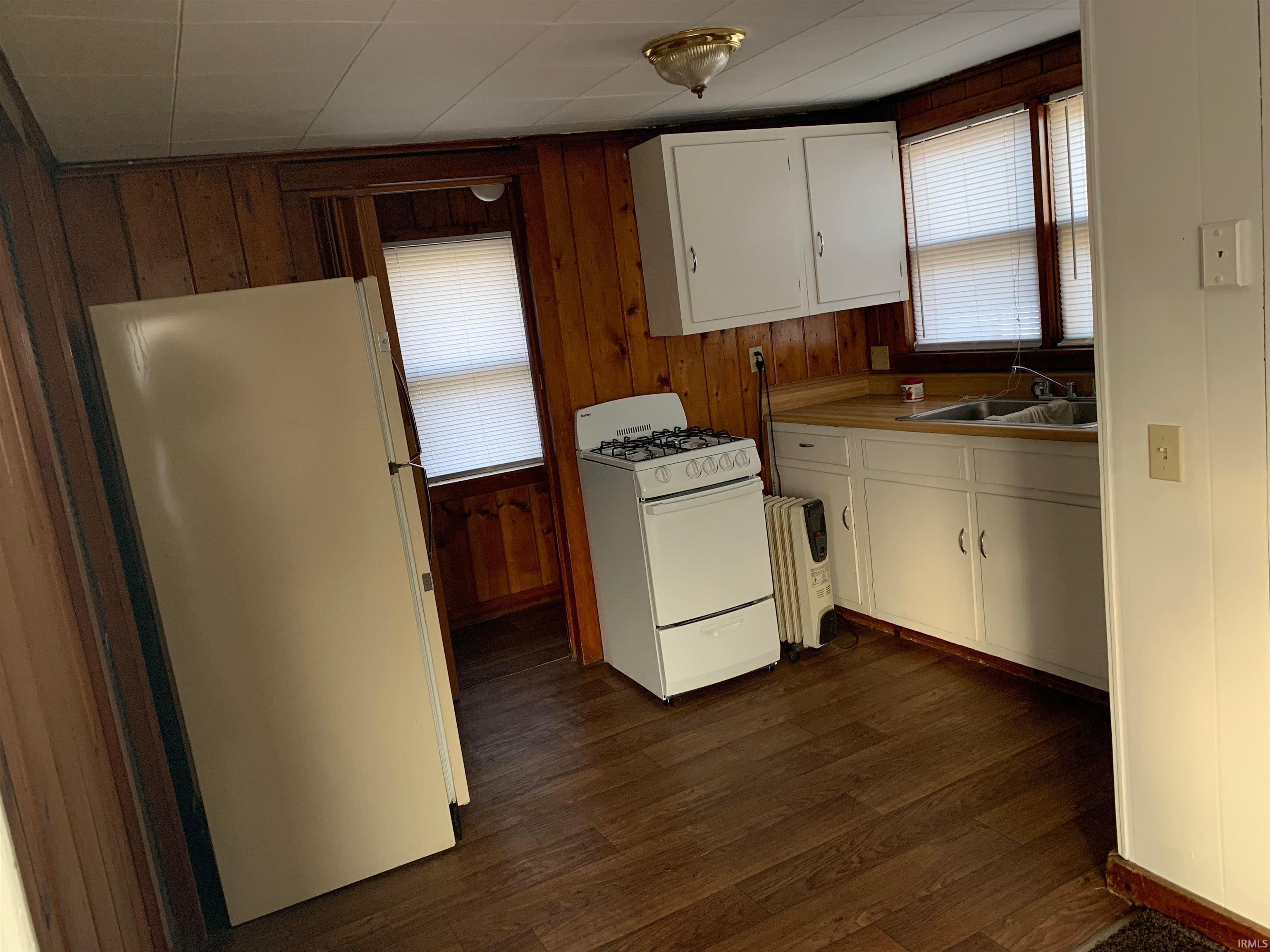 Compact kitchen featuring wood-finish flooring, wood paneling, white cabinetry, a double basin sink, and a four-burner range