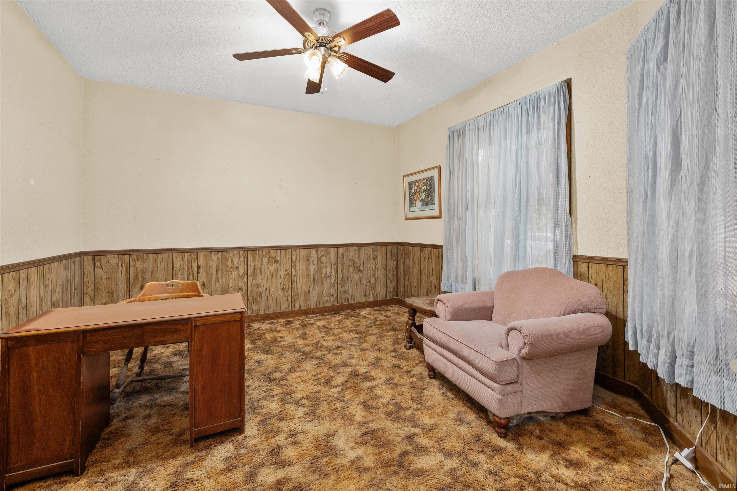 Room featuring wood paneling, light beige walls, and a ceiling fan with integrated lighting