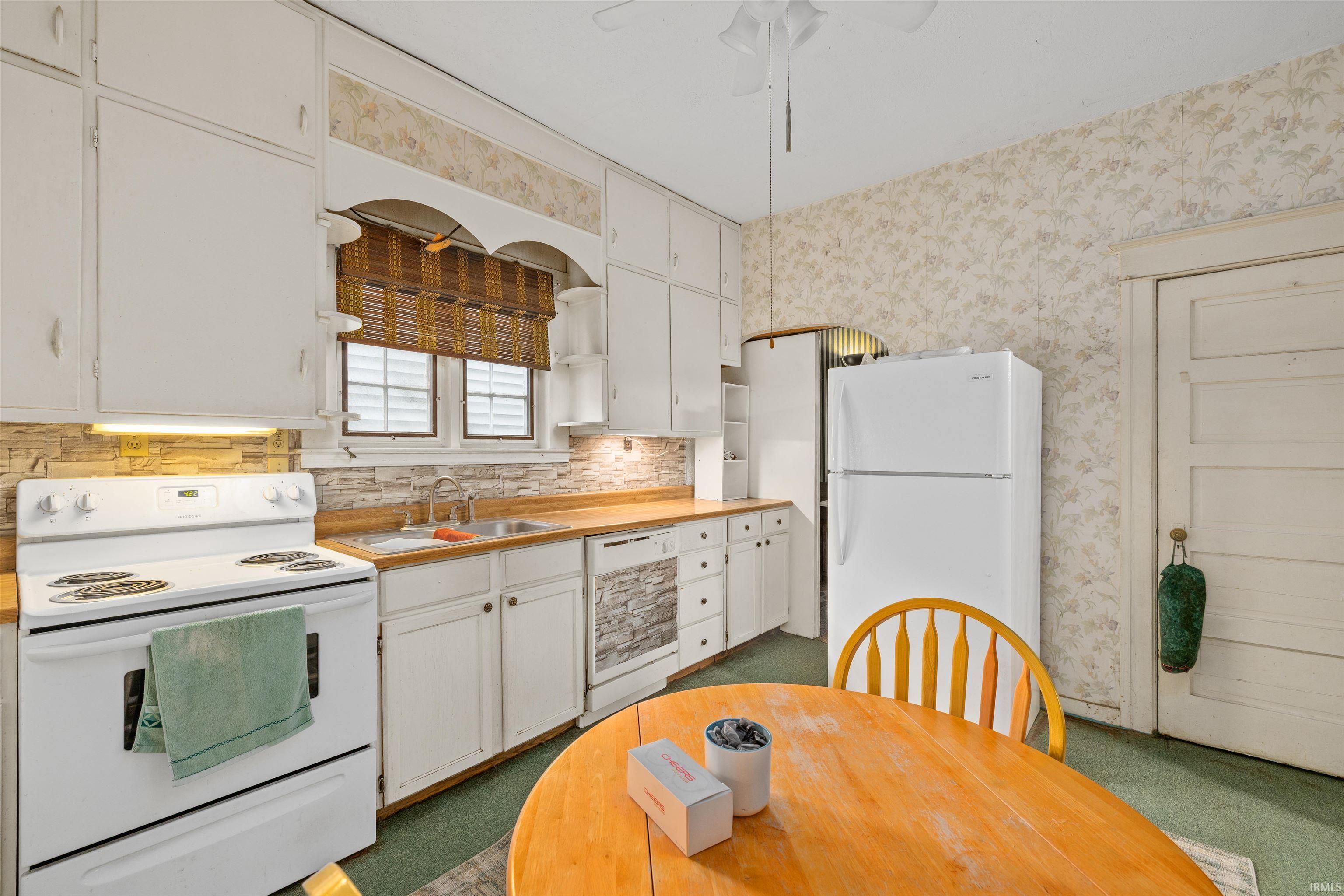 Kitchen featuring white cabinetry, wood-finish countertops, a stone-look backsplash, and a built-in double basin sink