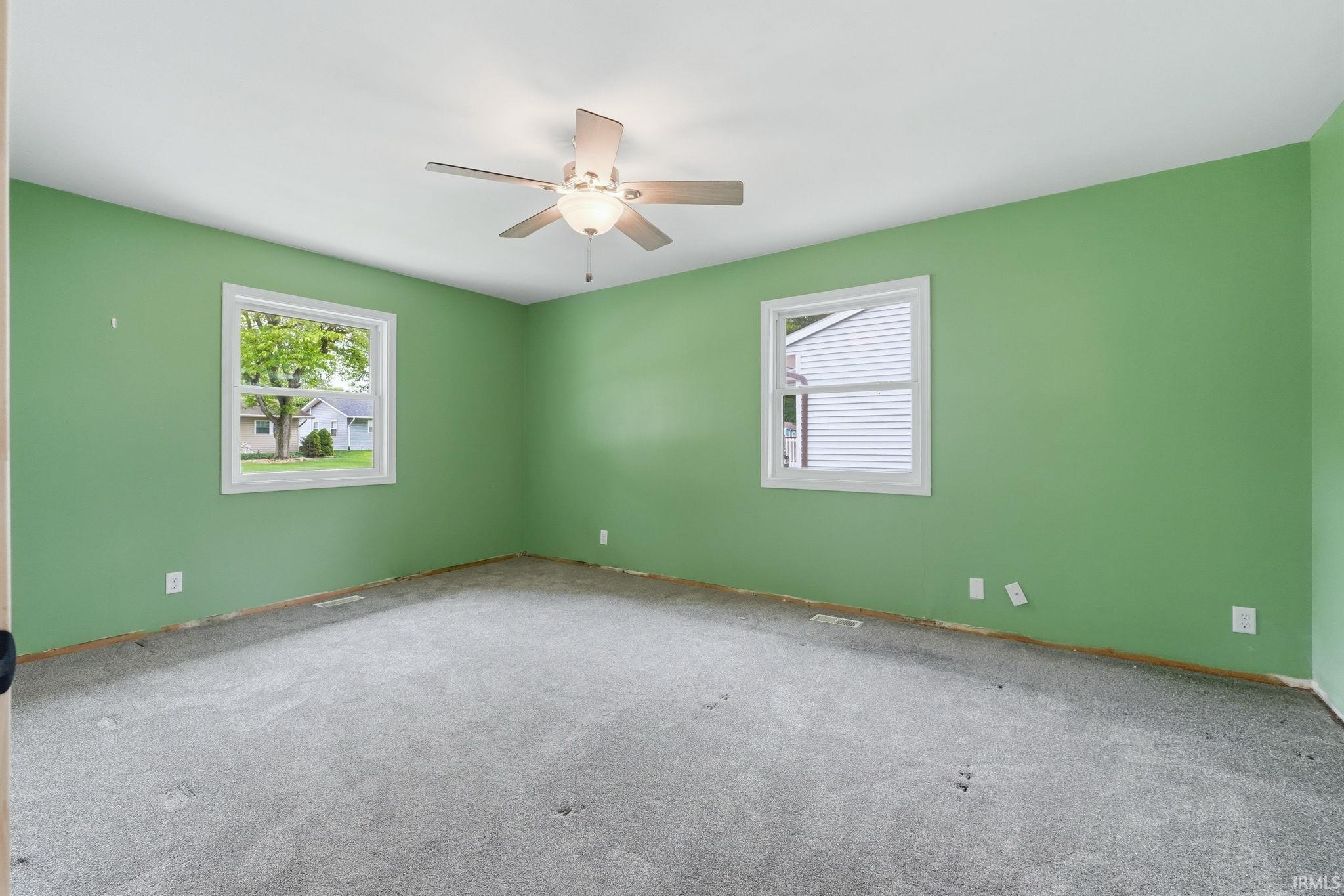 Spacious room featuring two windows, a ceiling fan with integrated lighting, and light green painted walls