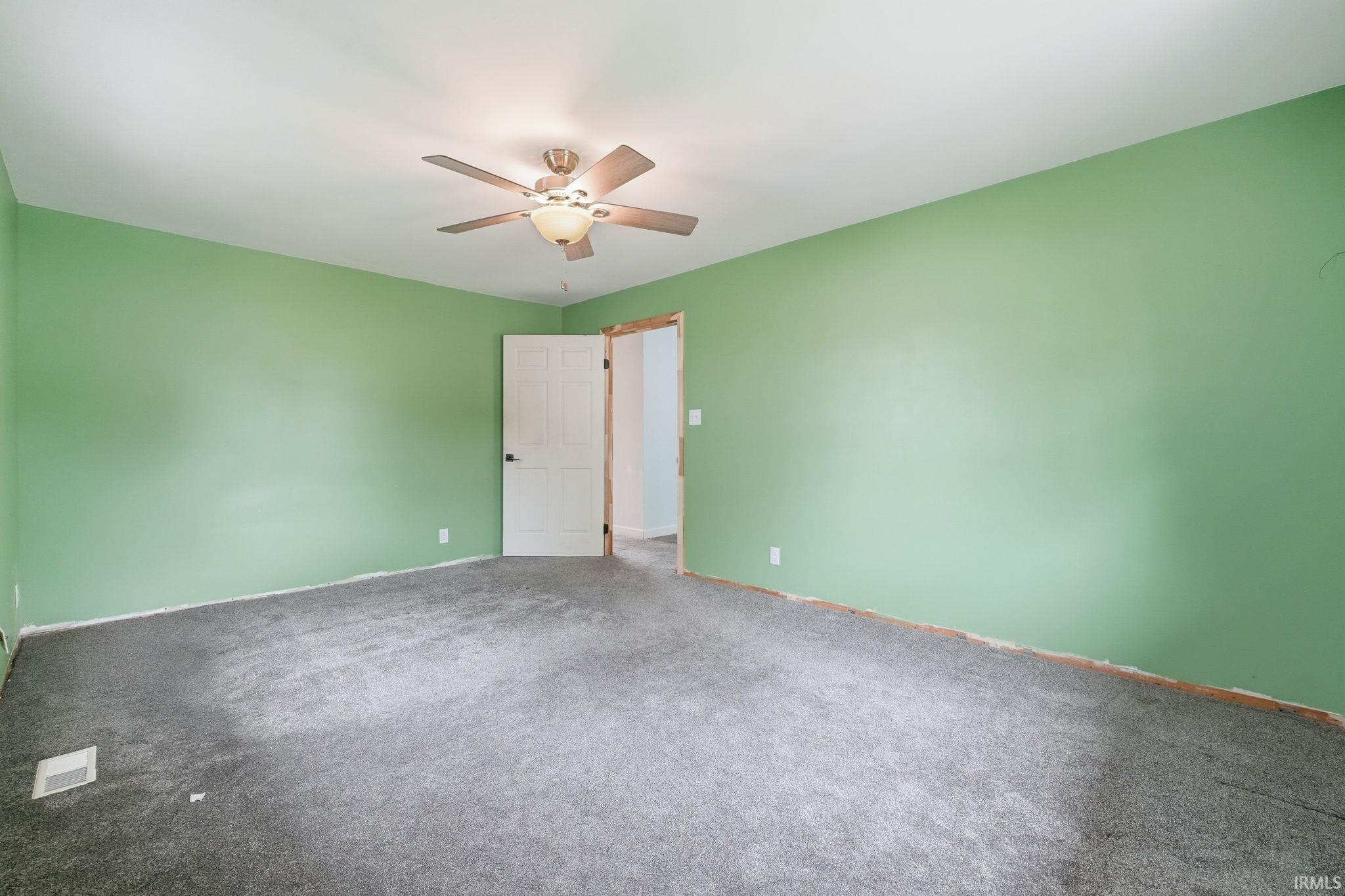 Spacious room featuring broadloom carpeting, light green wall paint, and a ceiling fan with integrated lighting