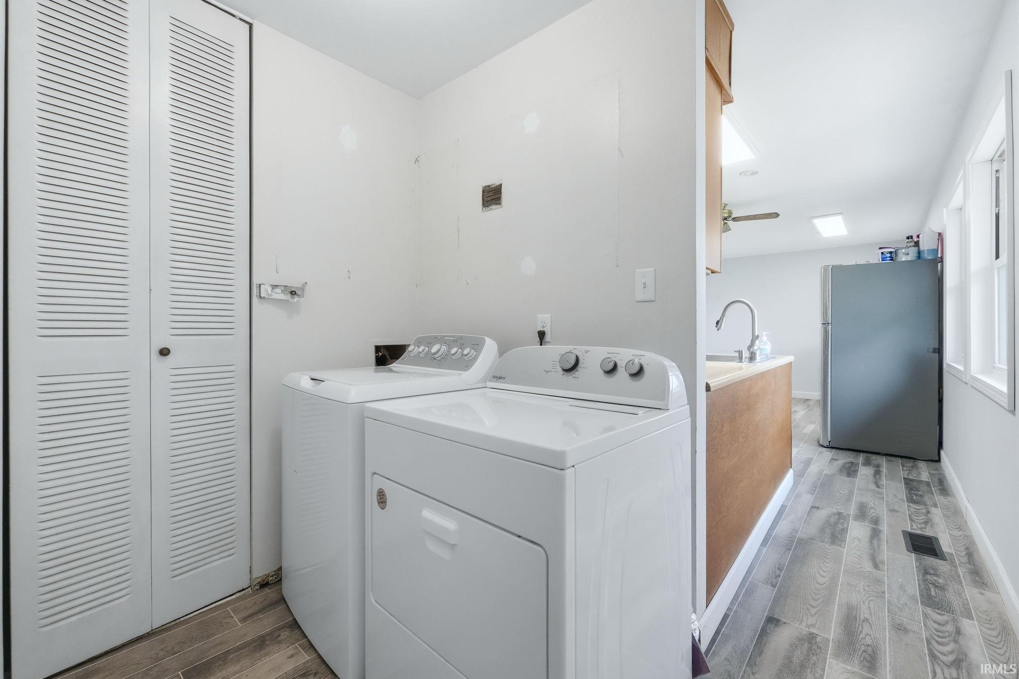 Dedicated laundry area featuring bifold louvered doors, wood-finish flooring, and light-toned walls