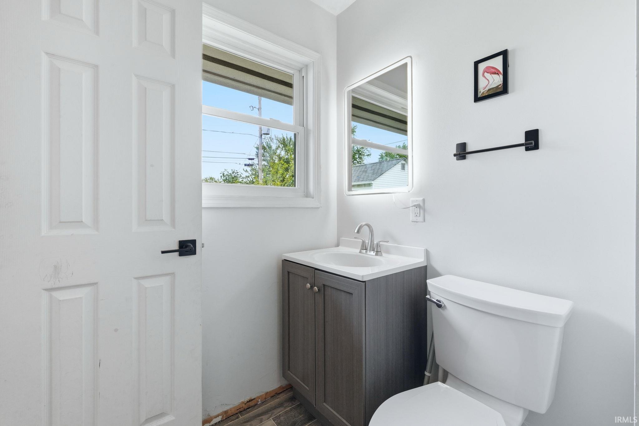 Bathroom featuring a gray vanity with a white countertop, a rectangular illuminated mirror, a window with exterior views, and a white toilet