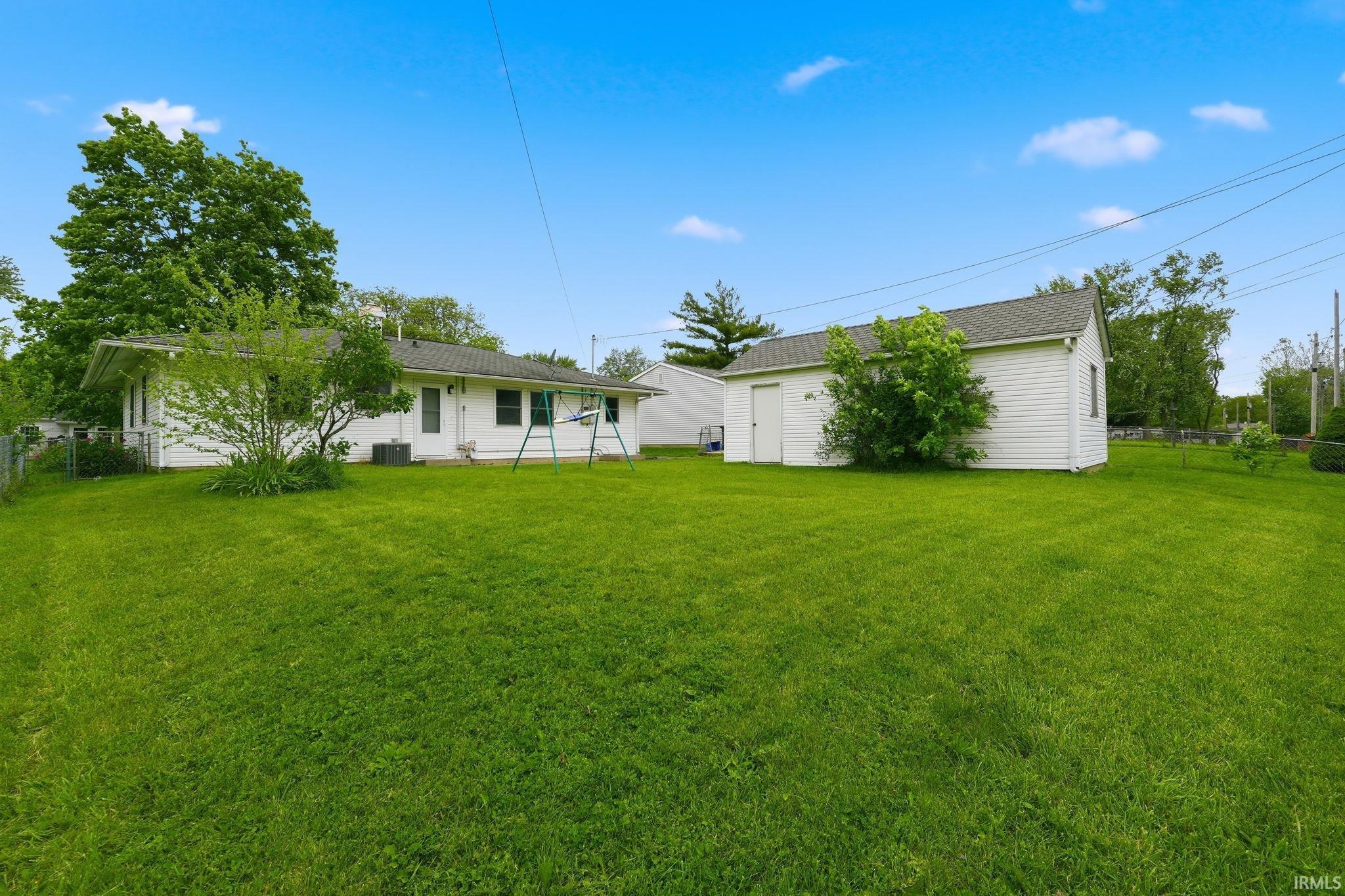 Expansive green lawn with a white detached shed and a single-story residence featuring white siding