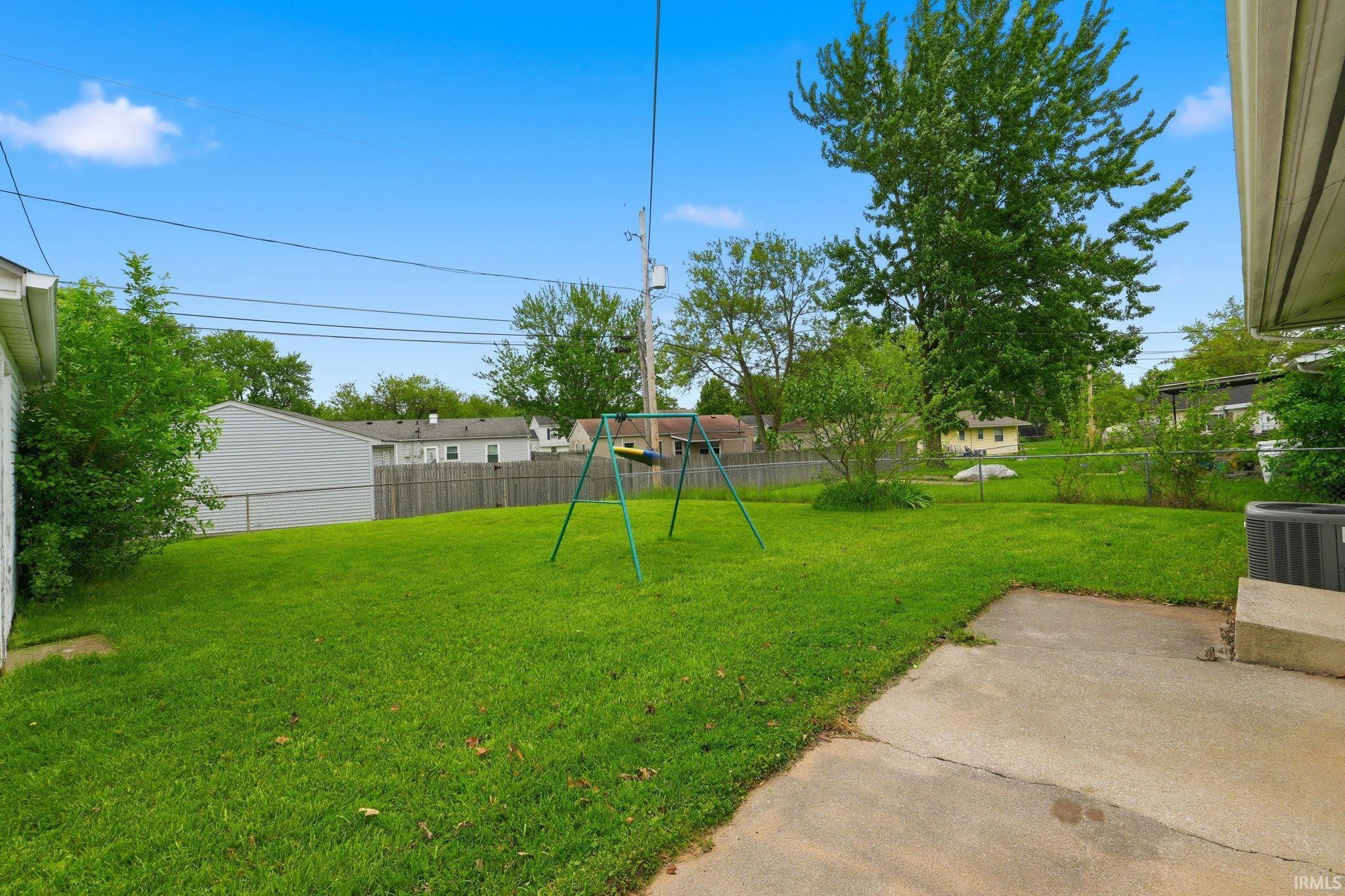 Expansive backyard featuring a lush lawn, mature trees, and a concrete patio area