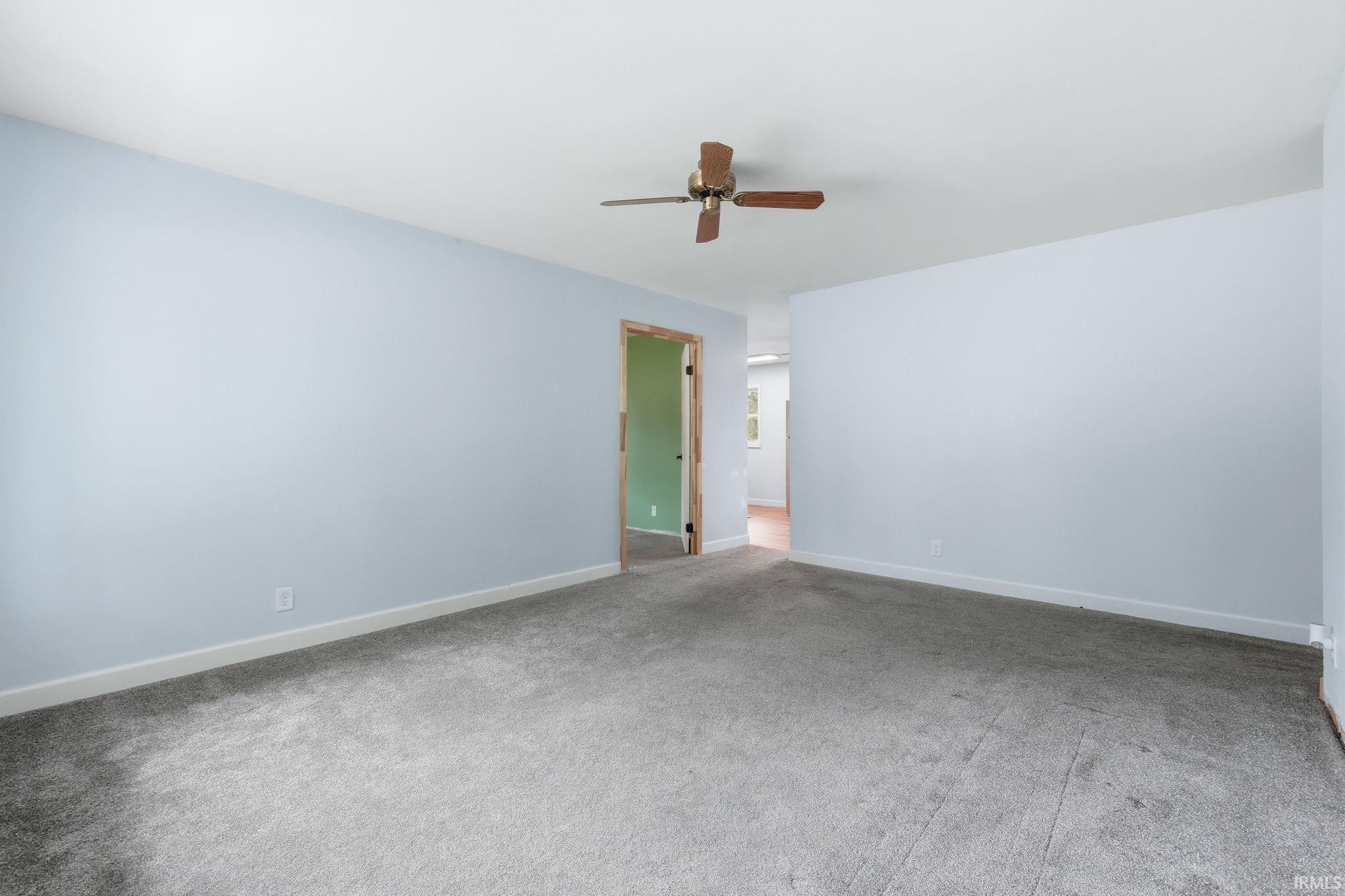 Spacious room with light blue painted walls, grey carpet flooring, and a ceiling fan with wooden blades