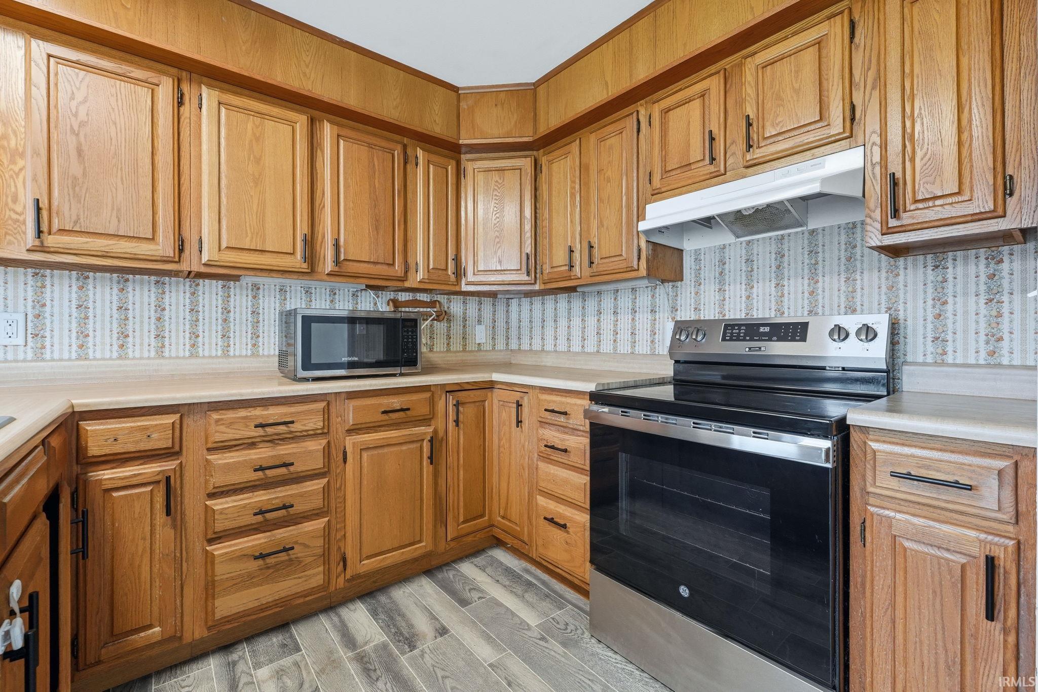 Kitchen featuring wood-finish cabinetry, laminate countertops, and a full suite of stainless steel appliances including a range with a smooth cooktop and a microwave