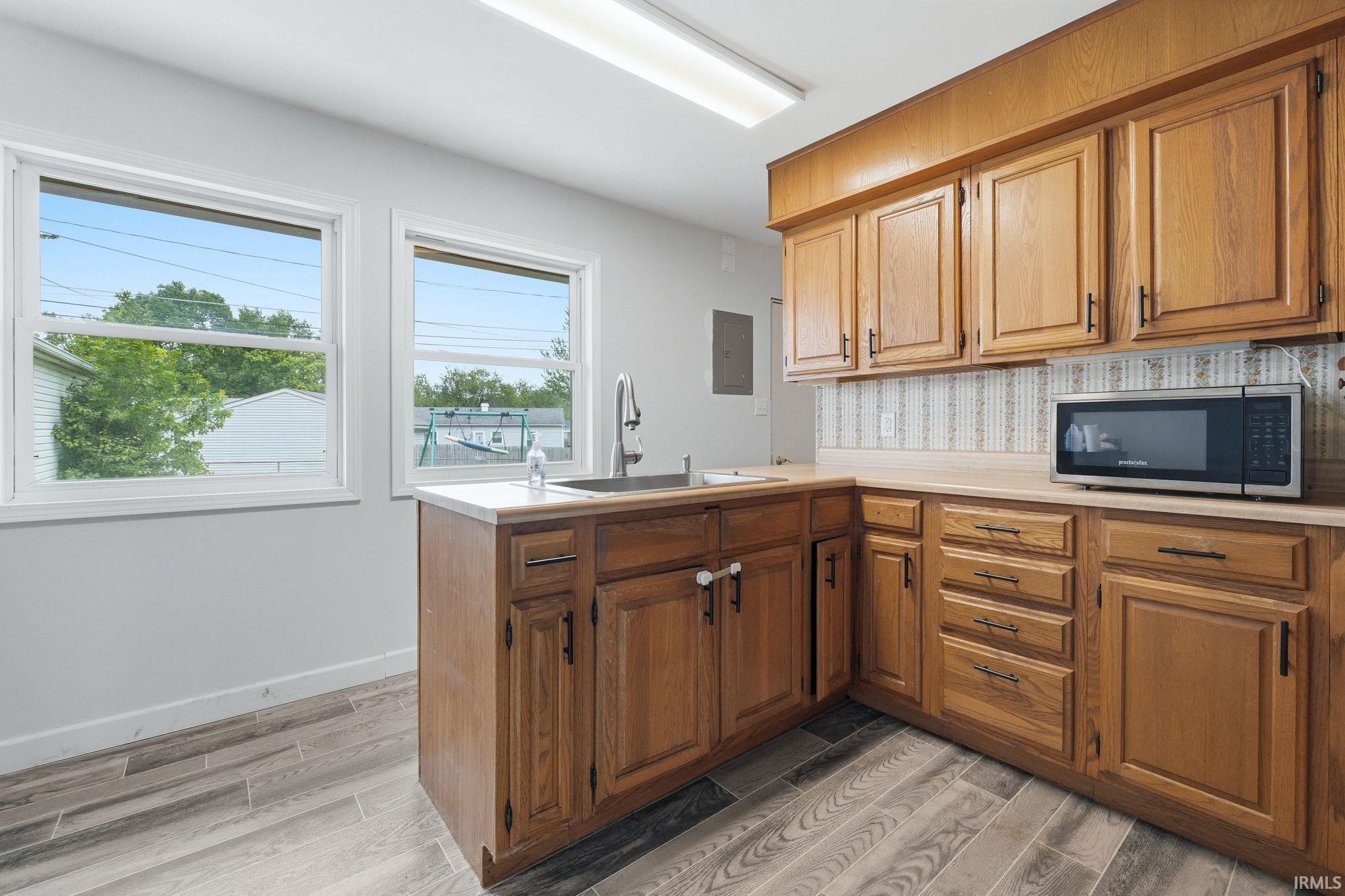 Kitchen featuring wood cabinetry, light-toned countertops, and two windows providing natural illumination