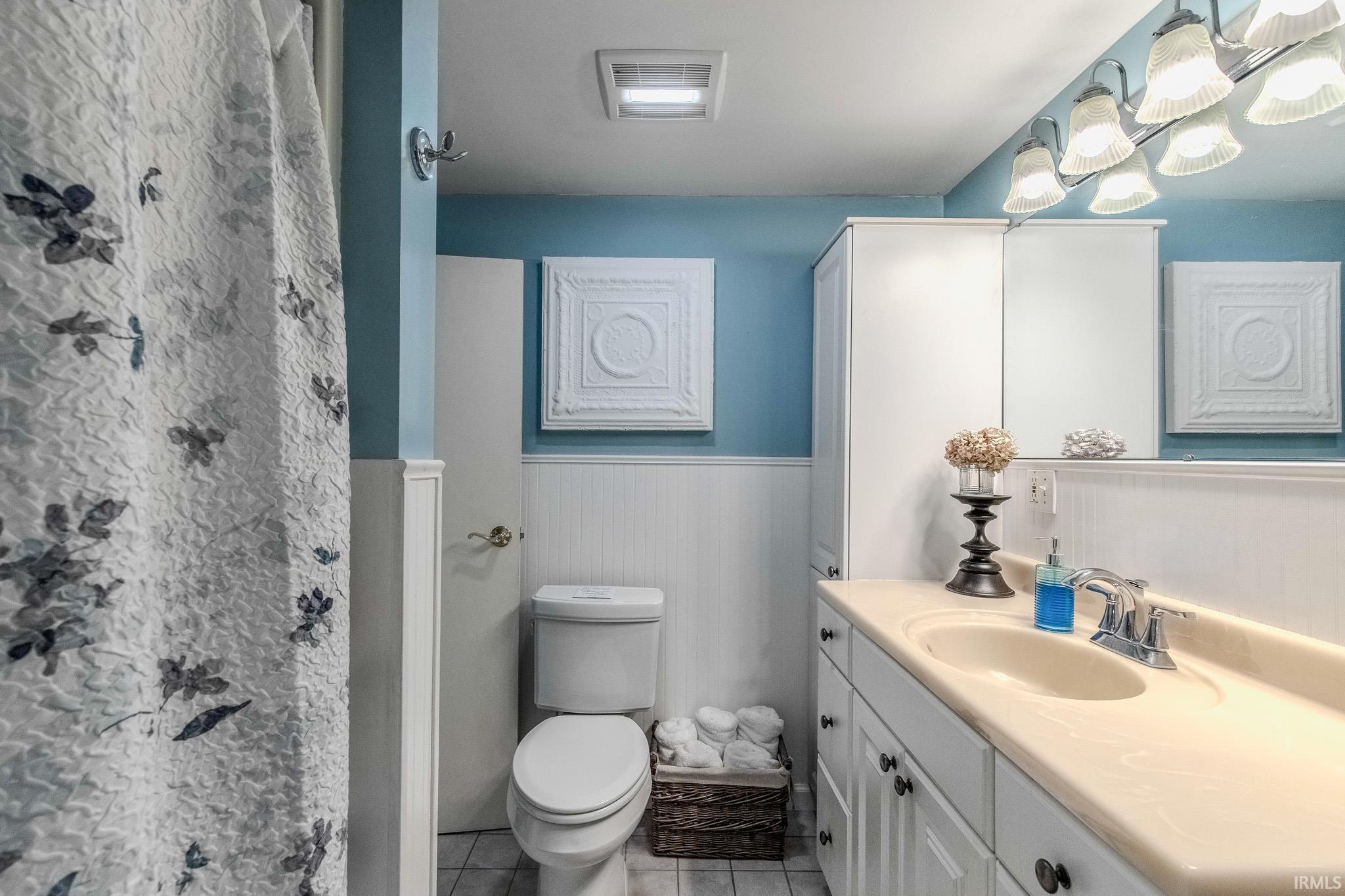 Bathroom featuring a single vanity with an integrated sink and chrome faucet, white cabinetry, beadboard wainscoting, and a white toilet