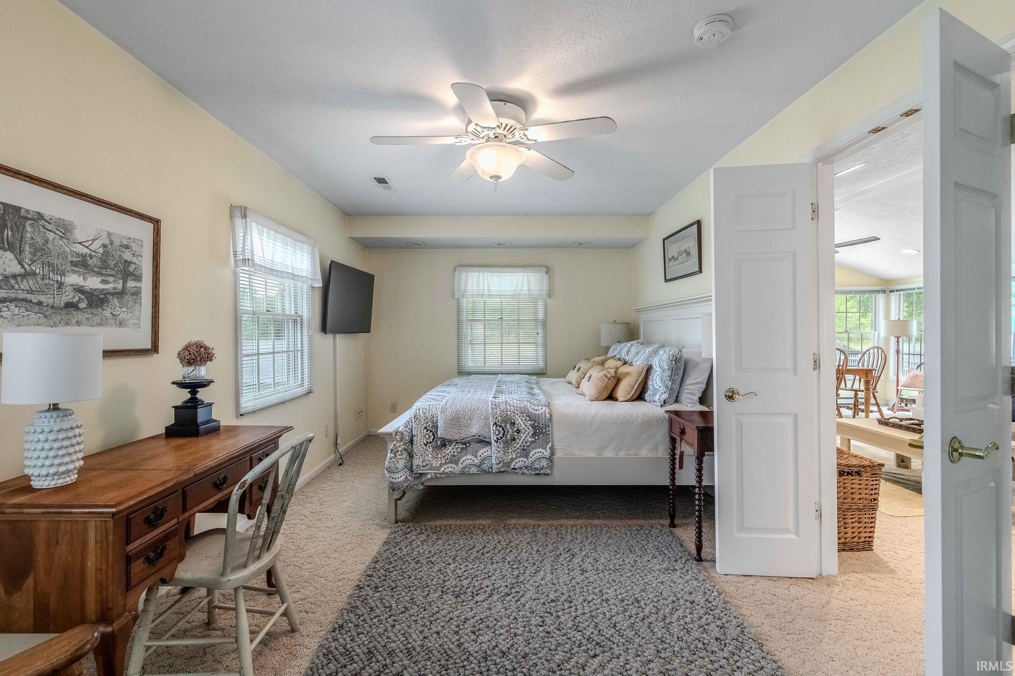 Carpeted room with a ceiling fan, two windows with blinds, a built-in mounted television, and a white paneled door