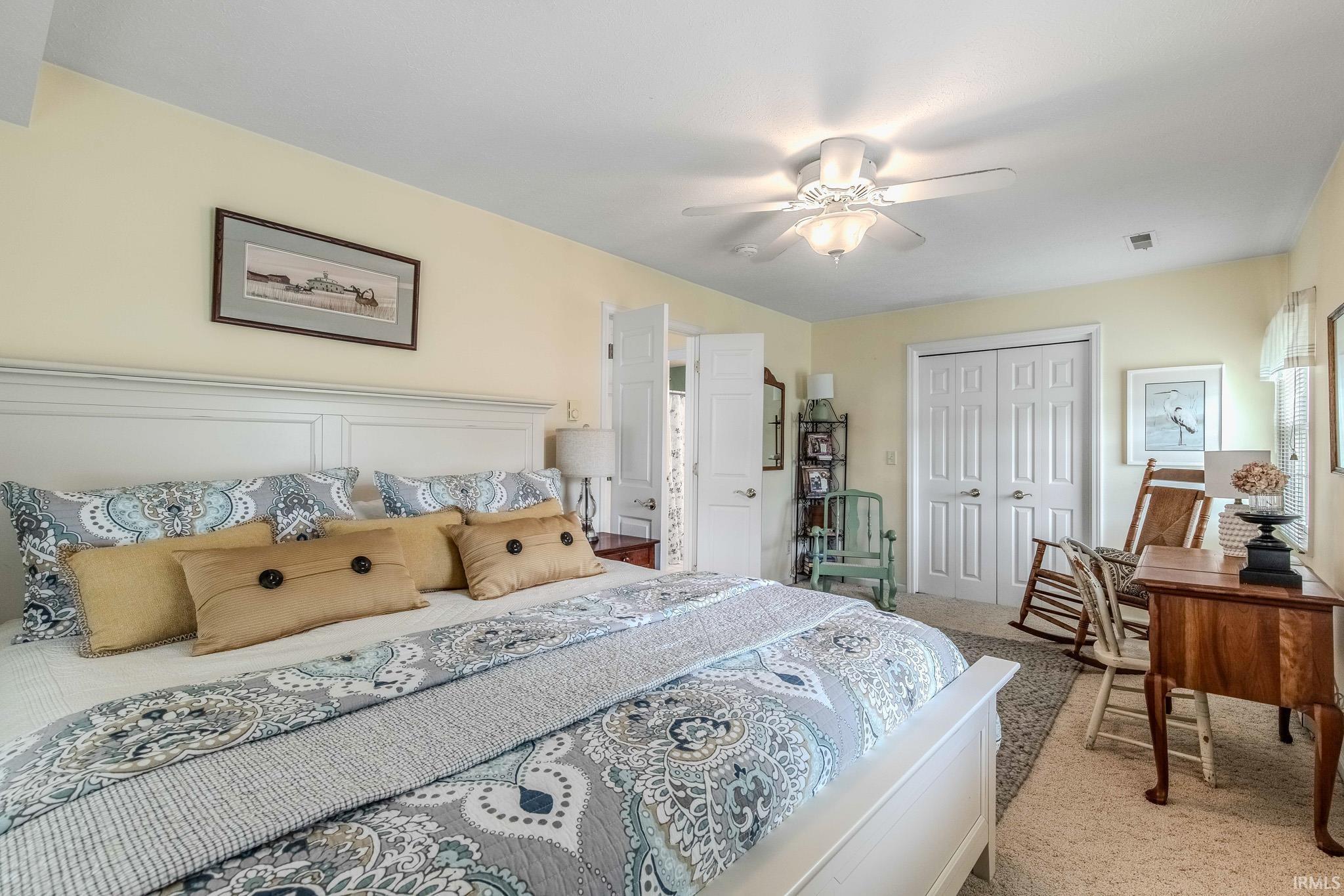 Bedroom featuring light yellow walls, a white paneled headboard, a ceiling fan with integrated lighting, and white bi-fold closet doors