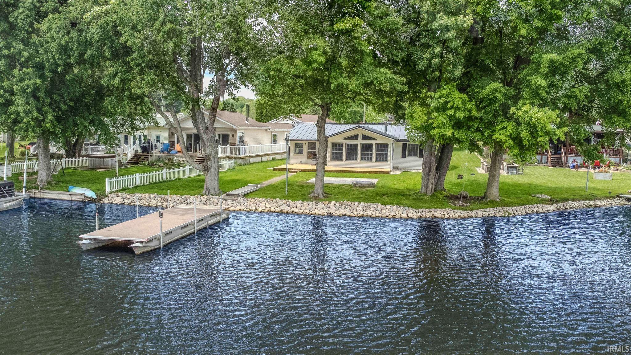 Waterfront property featuring a private dock, rocky shoreline, expansive lawn, and mature trees