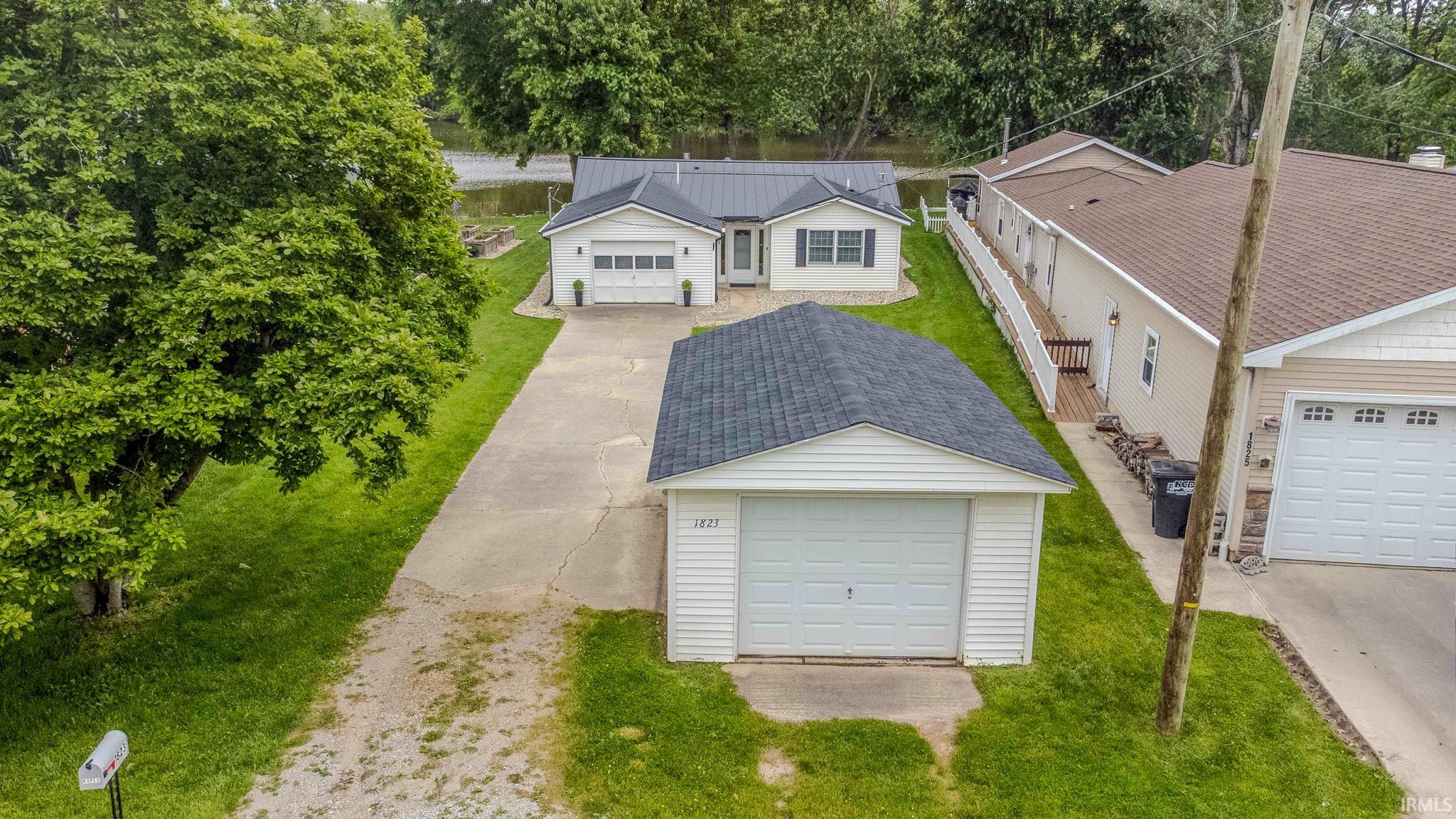Property featuring a detached garage, a long paved driveway, and a white siding exterior with a dark metal roof