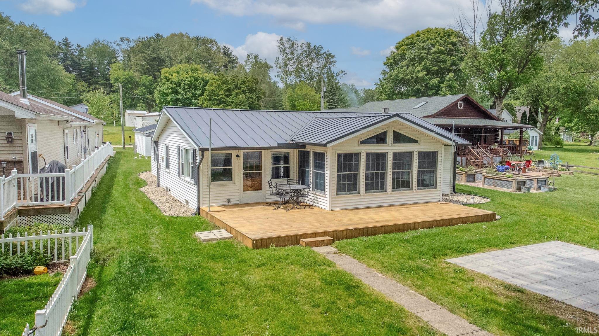 White siding exterior with a dark metal roof, sunroom extension, and a spacious wooden deck