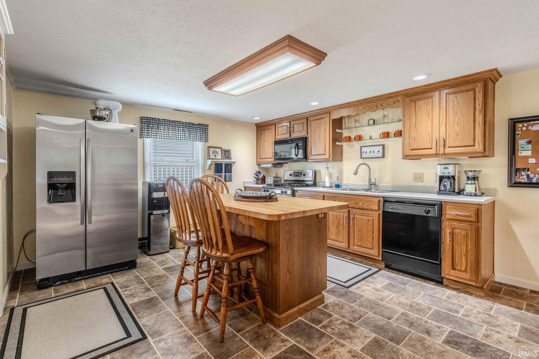 Kitchen featuring natural wood cabinetry, light countertops, a built-in oven, black dishwasher, and stainless steel refrigerator