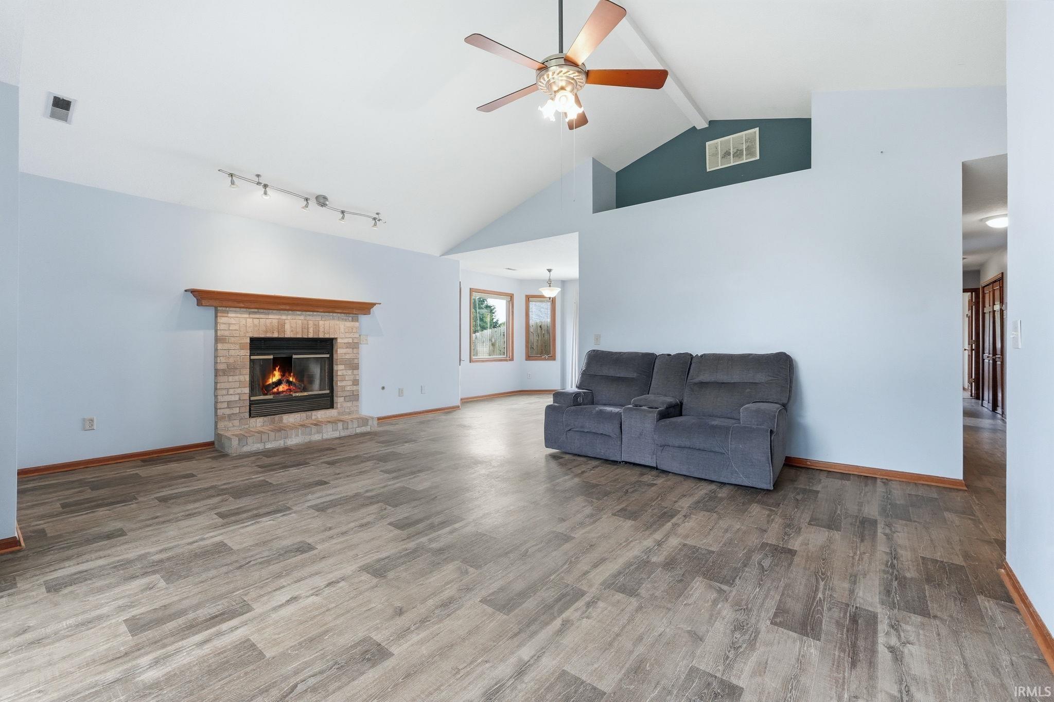 Living area featuring a brick fireplace with a wood mantle, vaulted ceiling with a ceiling fan, and wood-finish flooring
