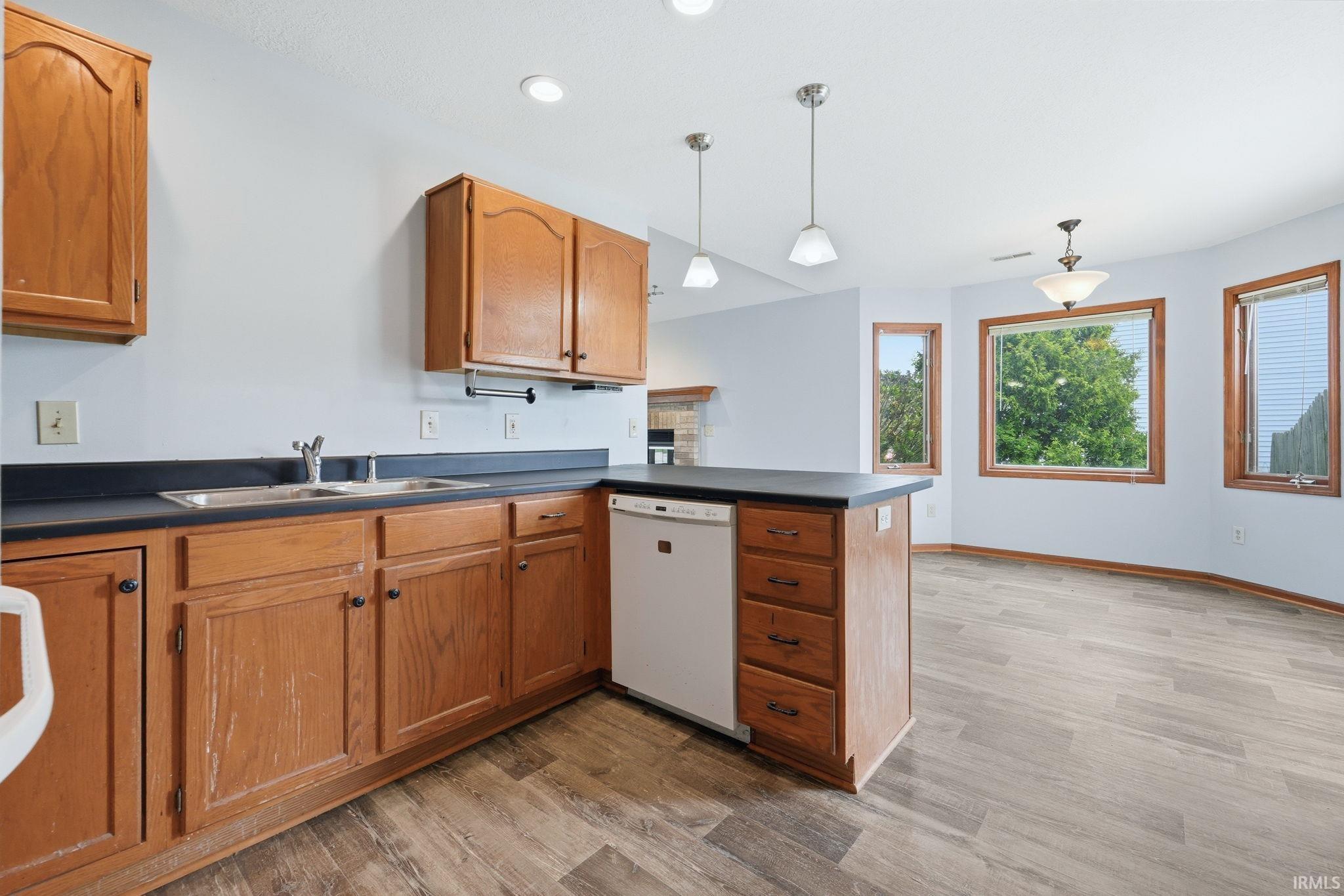 Kitchen featuring wood cabinetry, dark countertops, a double basin stainless steel sink, and a built-in dishwasher