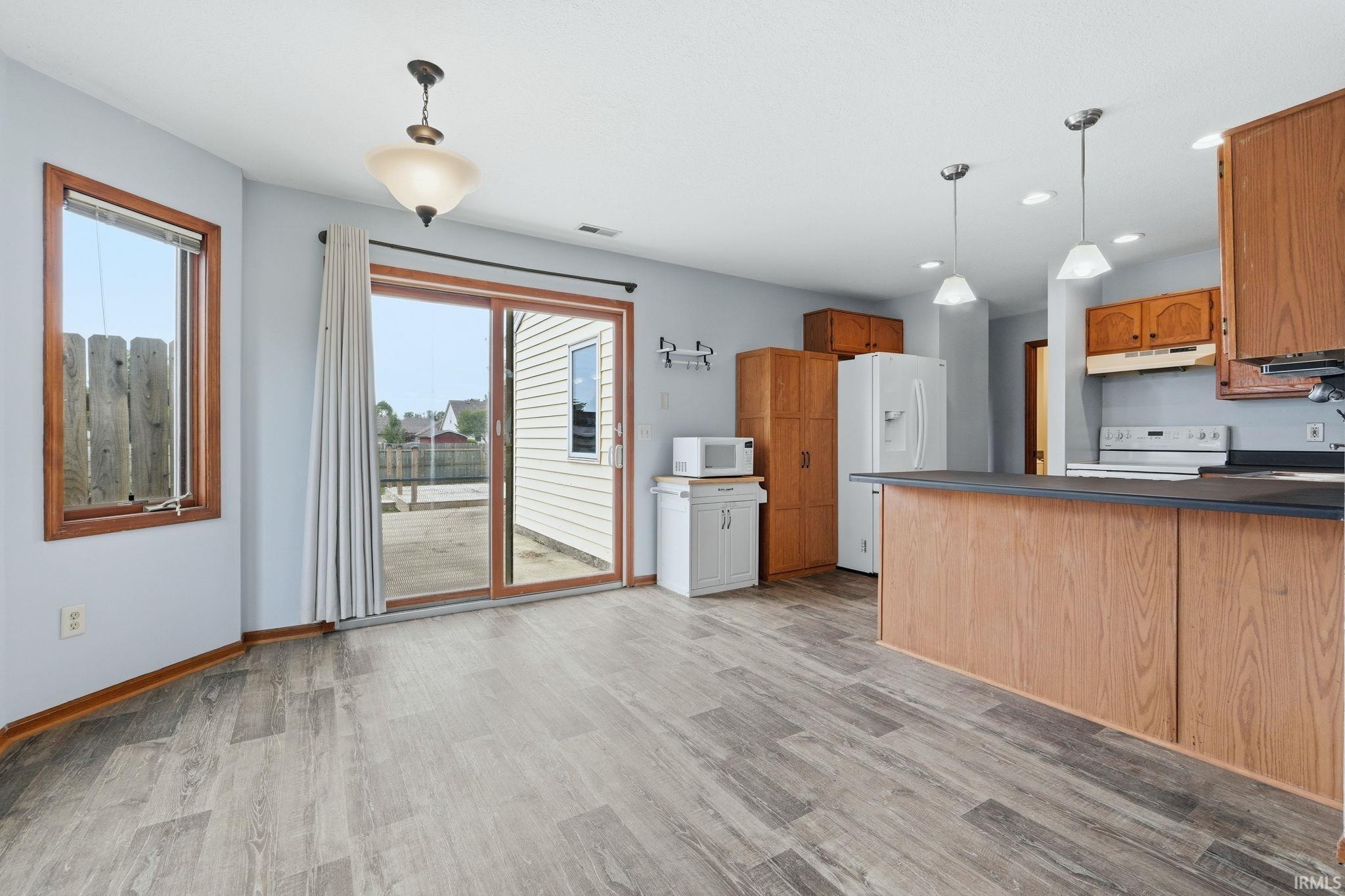 Open concept kitchen and dining area featuring wood-finish flooring, a sliding glass door, pendant lighting, and wood cabinetry