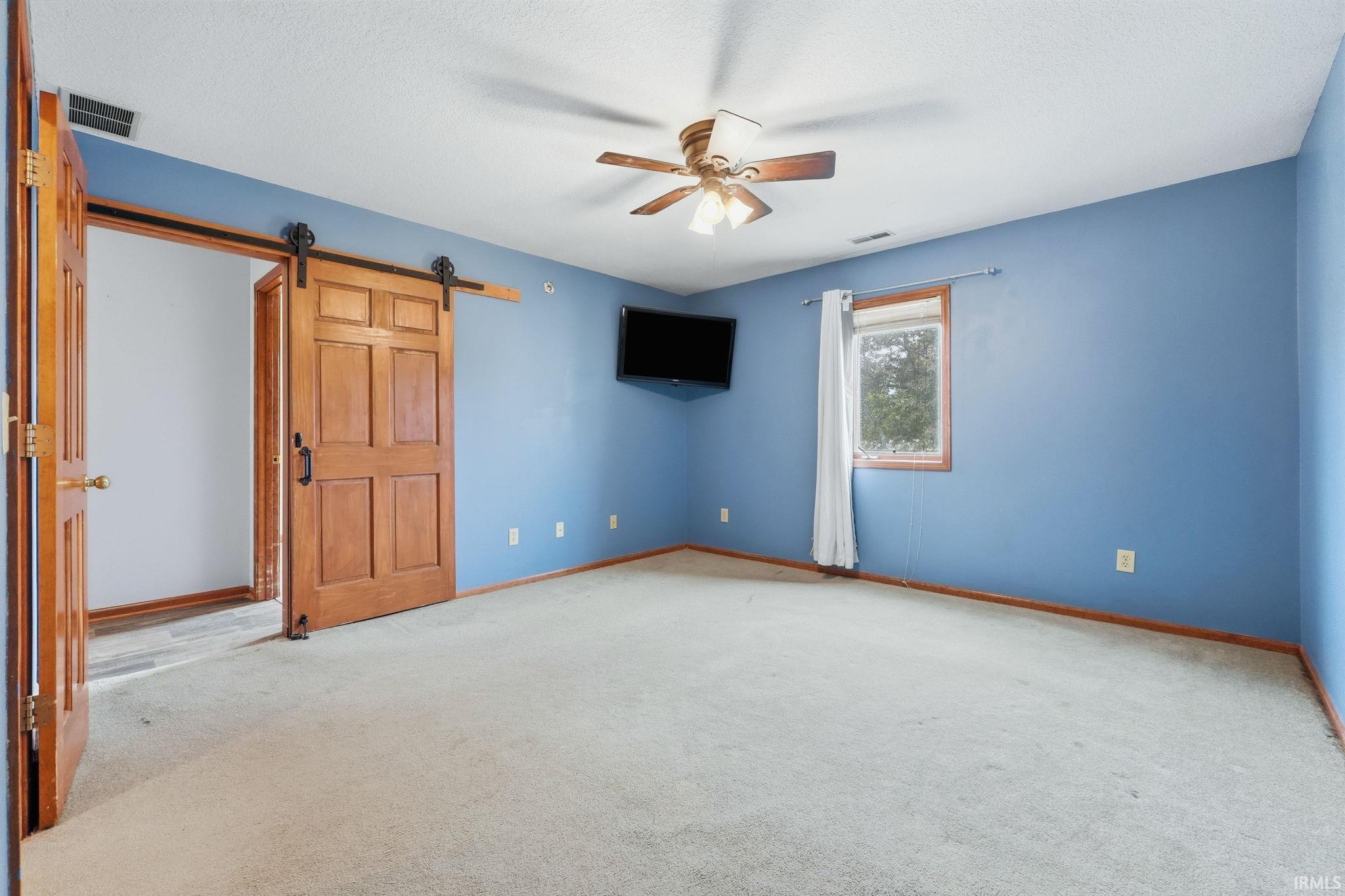 Spacious room featuring a ceiling fan, light-toned carpeting, and a wood-framed window