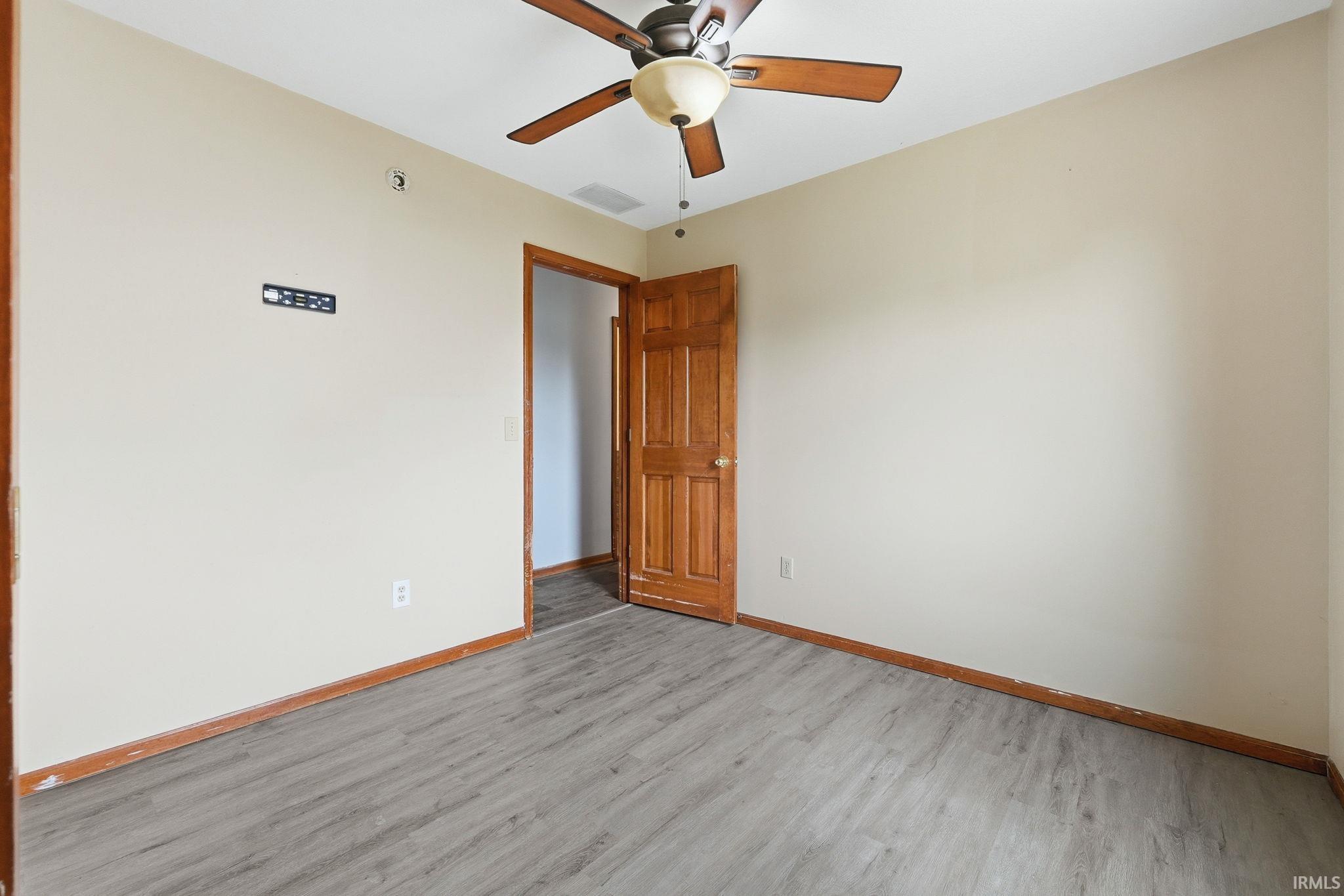 Neutral wall color, wood-finish flooring, wood trim, wood door, and a ceiling fan with light fixture