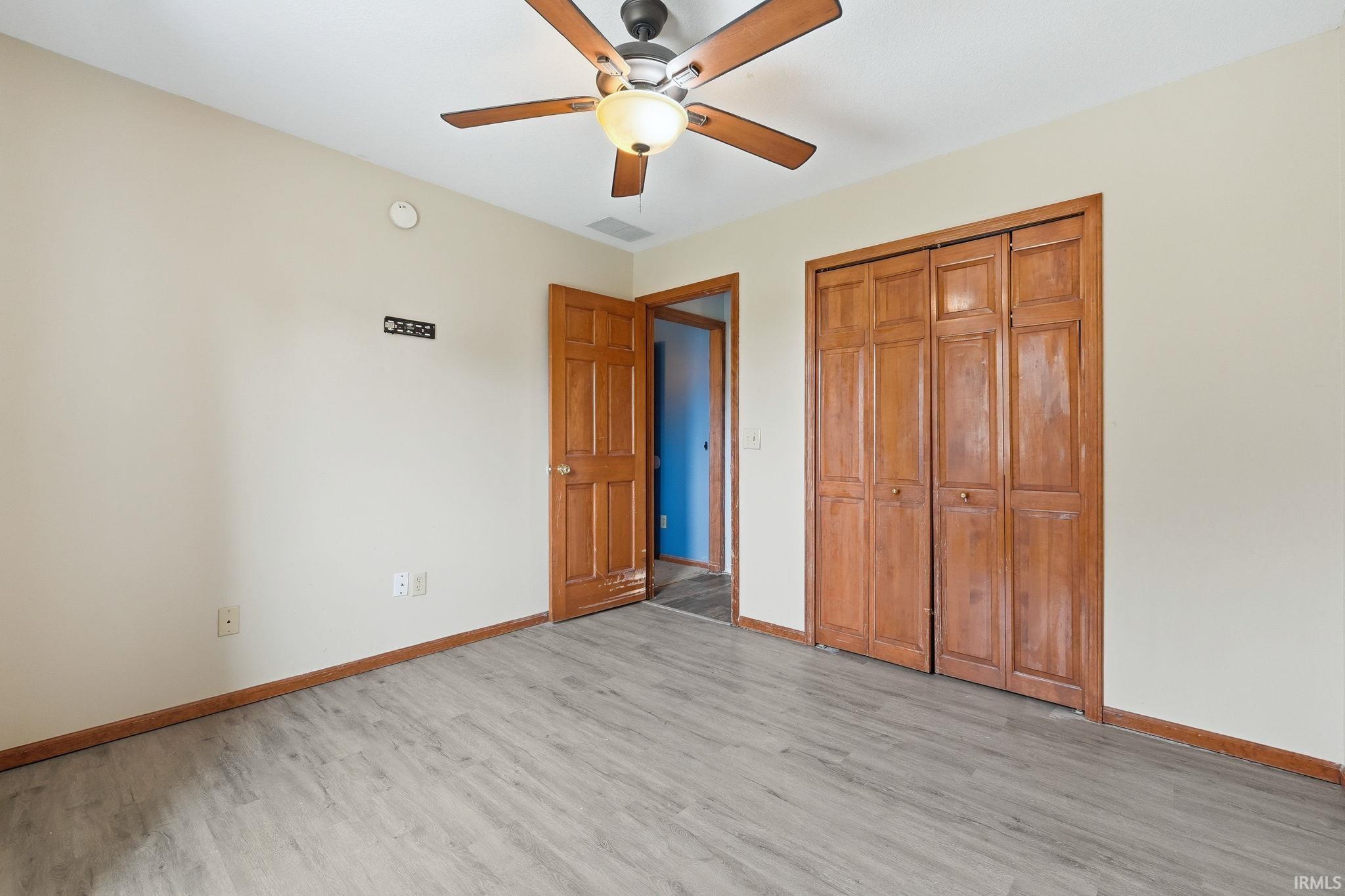 Room featuring wood-finish flooring, a ceiling fan with integrated lighting, and a closet with bifold wood doors
