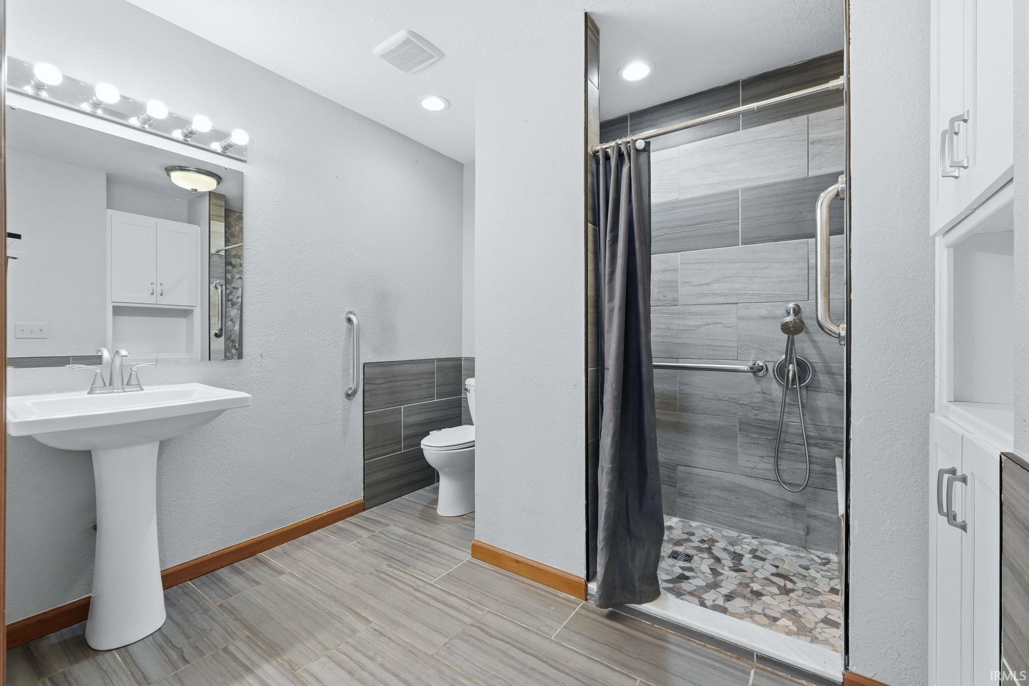 Full bathroom featuring a pedestal sink, wood-finish flooring, a tiled shower with a pebble floor, and built-in white cabinetry