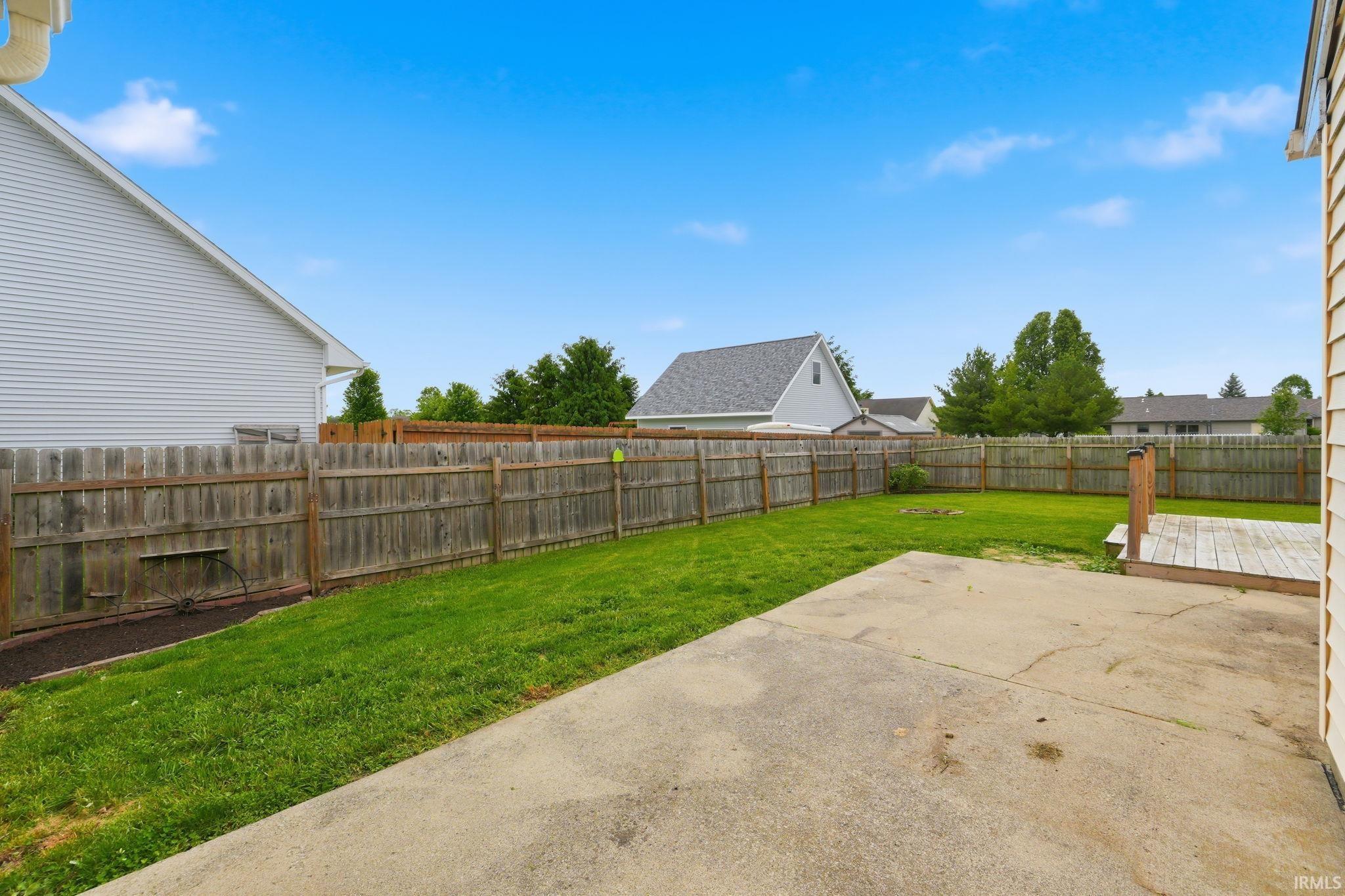 Expansive backyard featuring a concrete patio, wood deck, and wood privacy fencing enclosing a green lawn