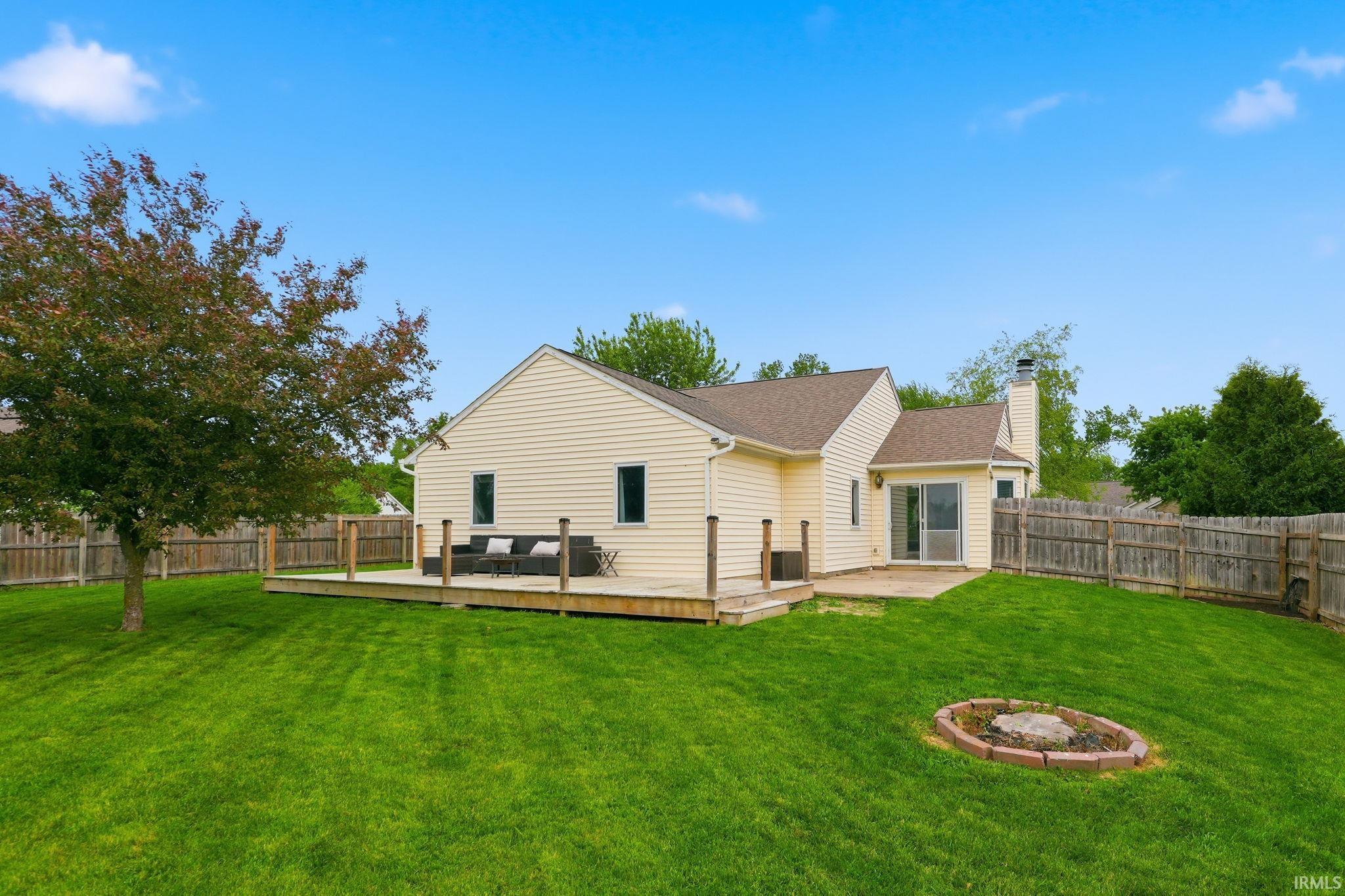 Expansive backyard featuring a large wooden deck, a concrete patio, and a stone-ringed fire pit