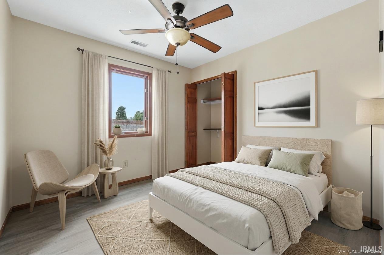 Bedroom featuring wood-finish flooring, a window with wood trim, and a ceiling fan with integrated lighting