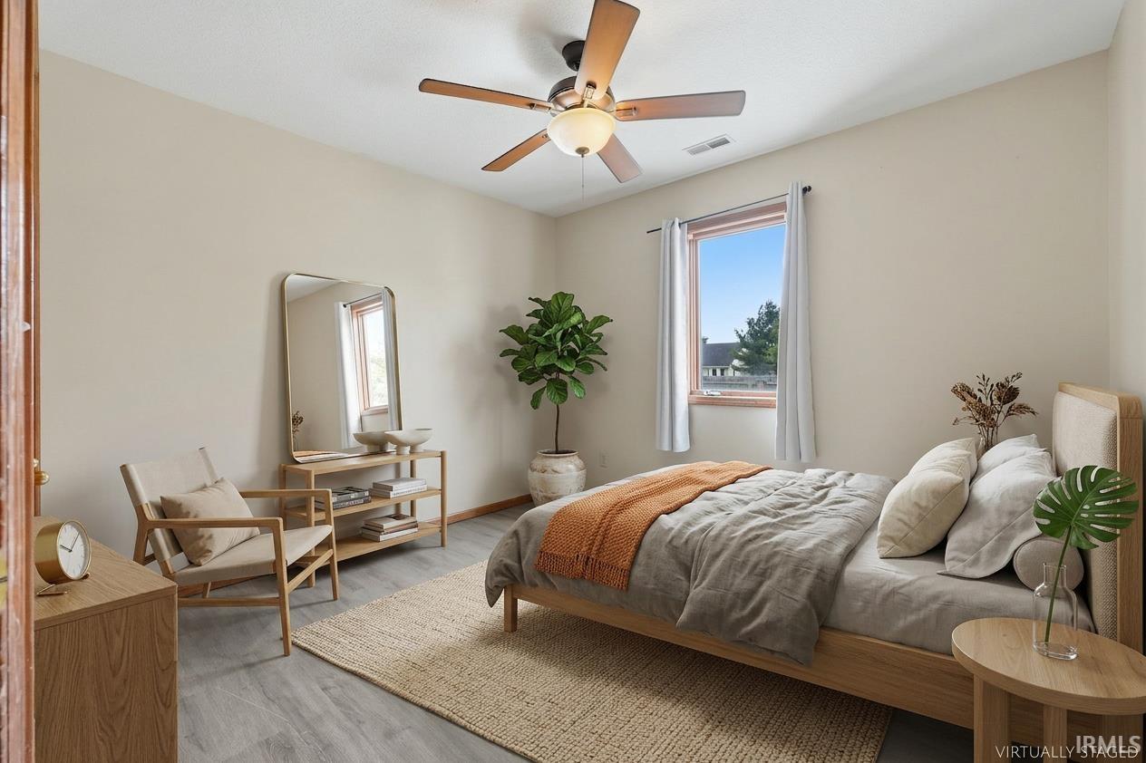Bedroom featuring a ceiling fan with integrated lighting, a window with exterior views, and wood-finish flooring