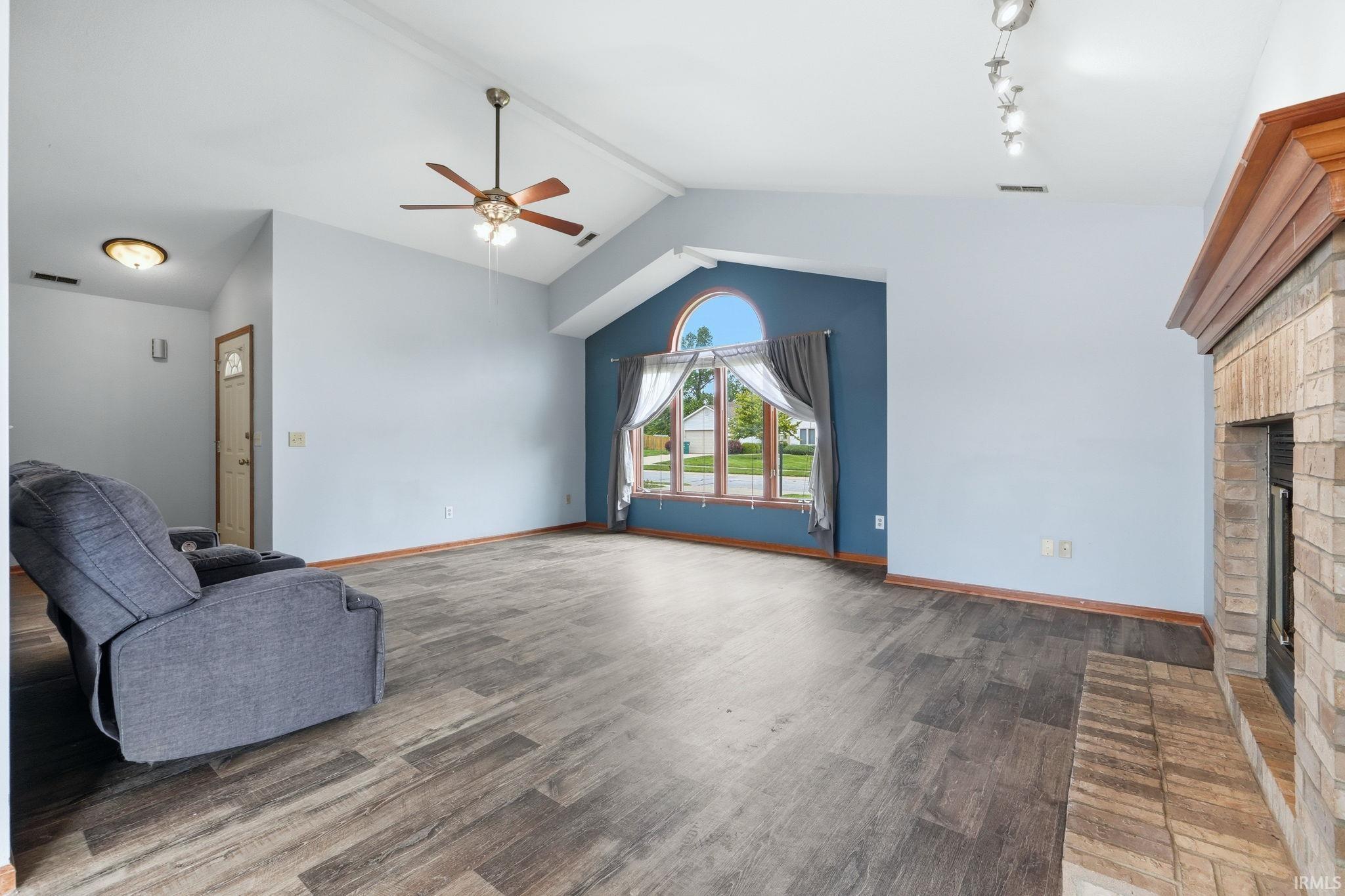 Spacious living area featuring vaulted ceilings, wood-finish flooring, a ceiling fan, and a stone fireplace with a substantial wood mantel