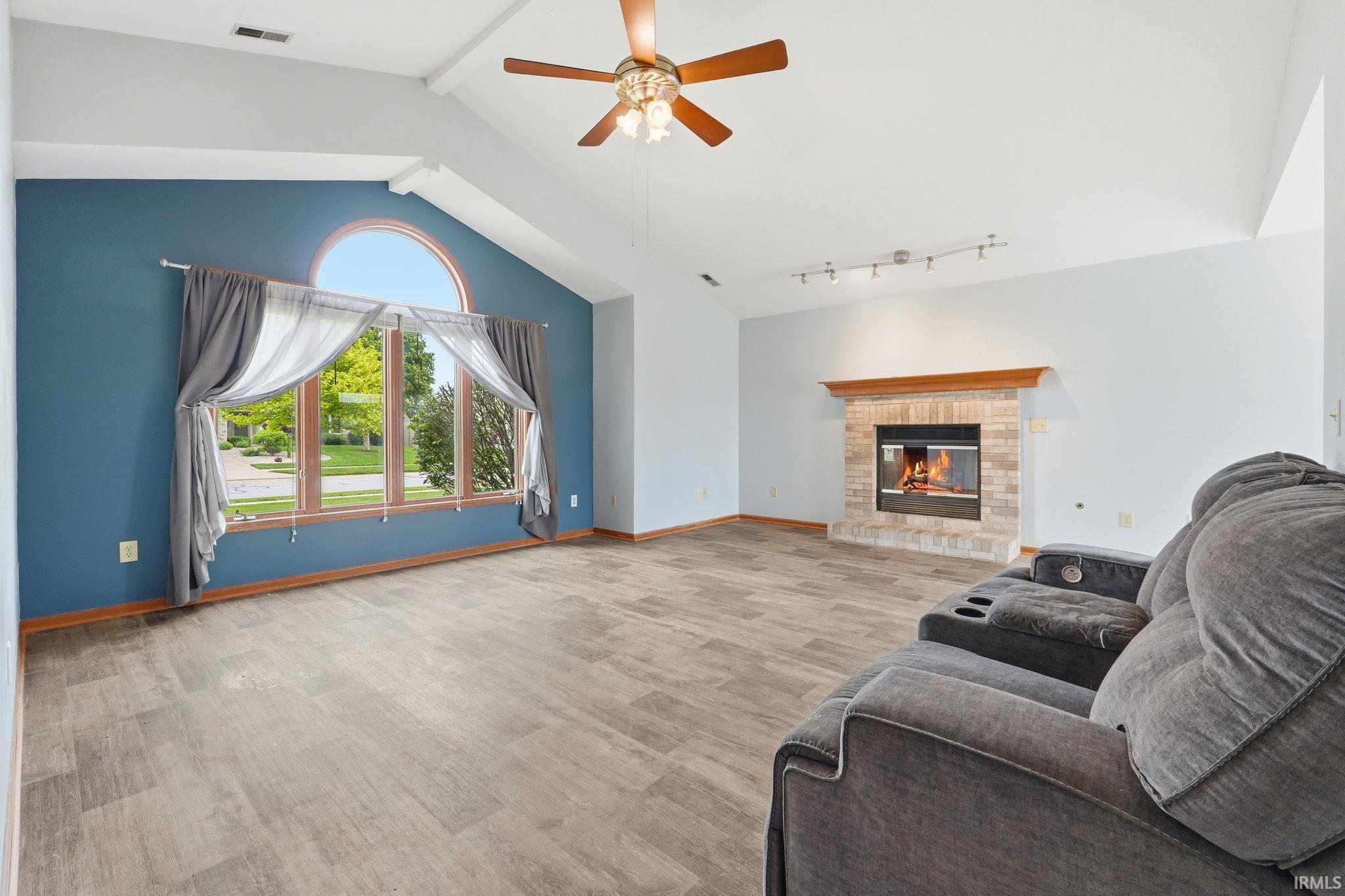 Living area featuring vaulted ceilings, wood-finish flooring, and a brick fireplace with a wood mantel