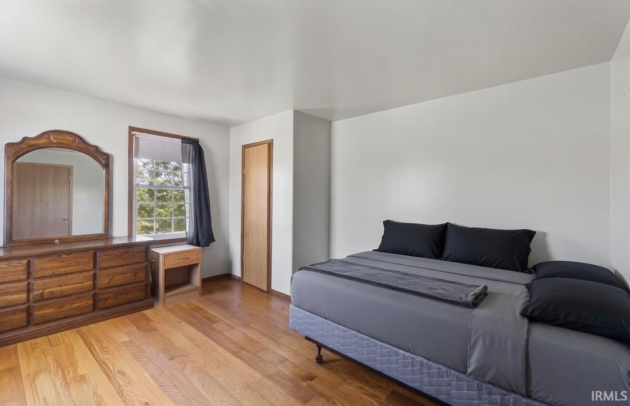 Bright room featuring wood-finish flooring, white walls, and a window with a wooded outlook
