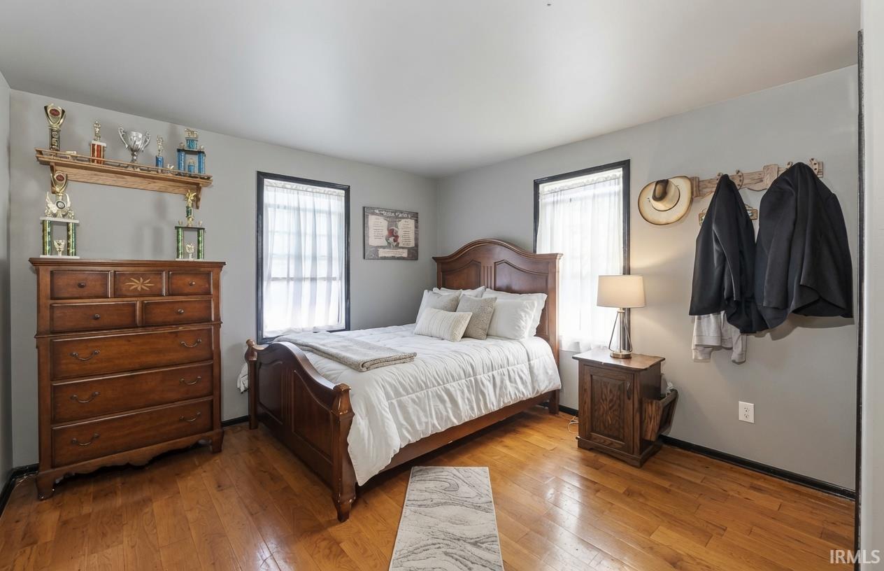 Bedroom featuring wood-finish flooring, two windows with white sheer coverings, and light gray wall paint