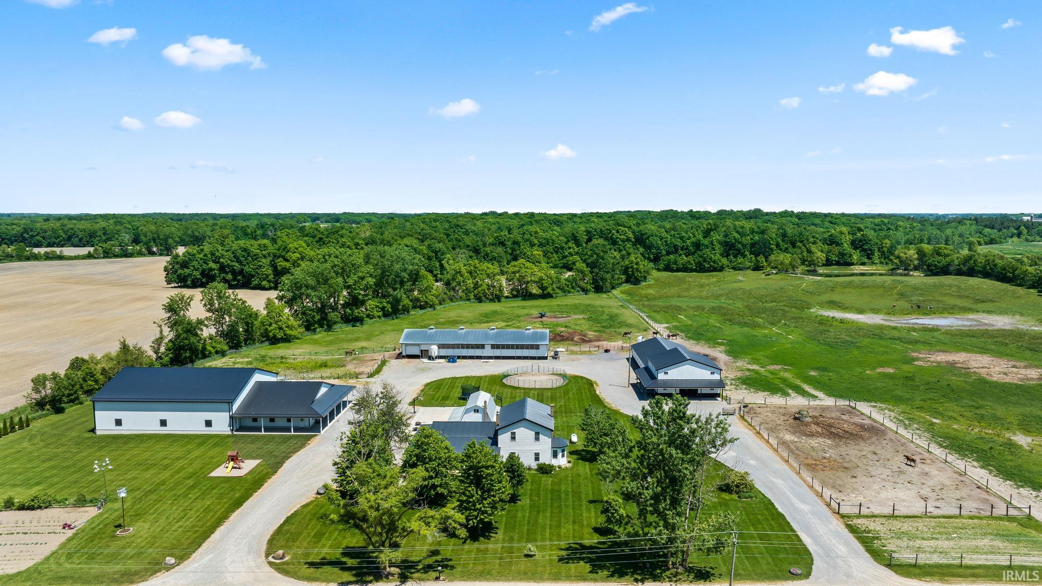 Expansive rural property featuring a white residence, multiple outbuildings with dark roofs, a fenced paddock, and substantial open fields