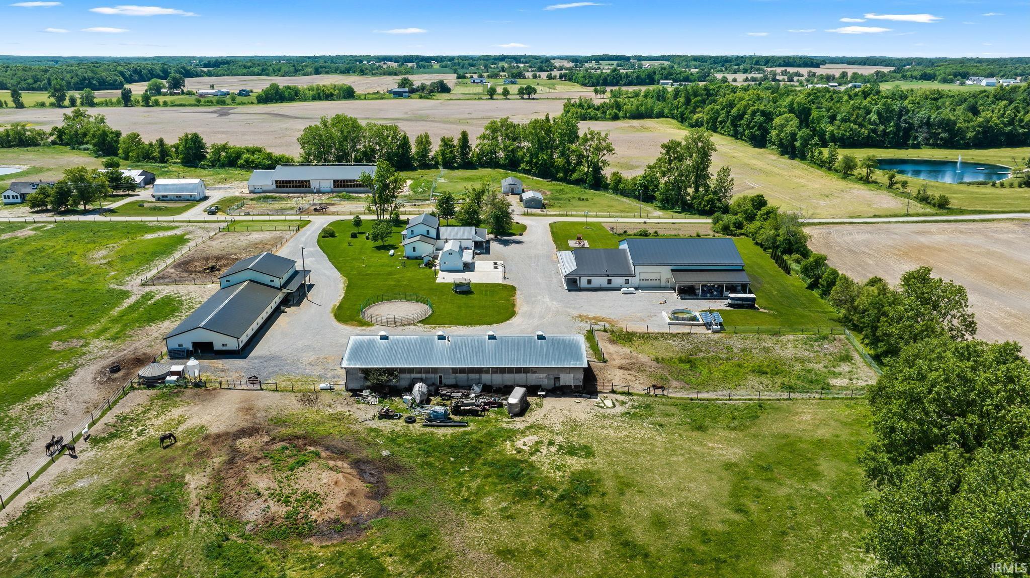 Expansive rural property featuring multiple outbuildings, fenced paddocks, a gravel driveway, and a pond with a fountain