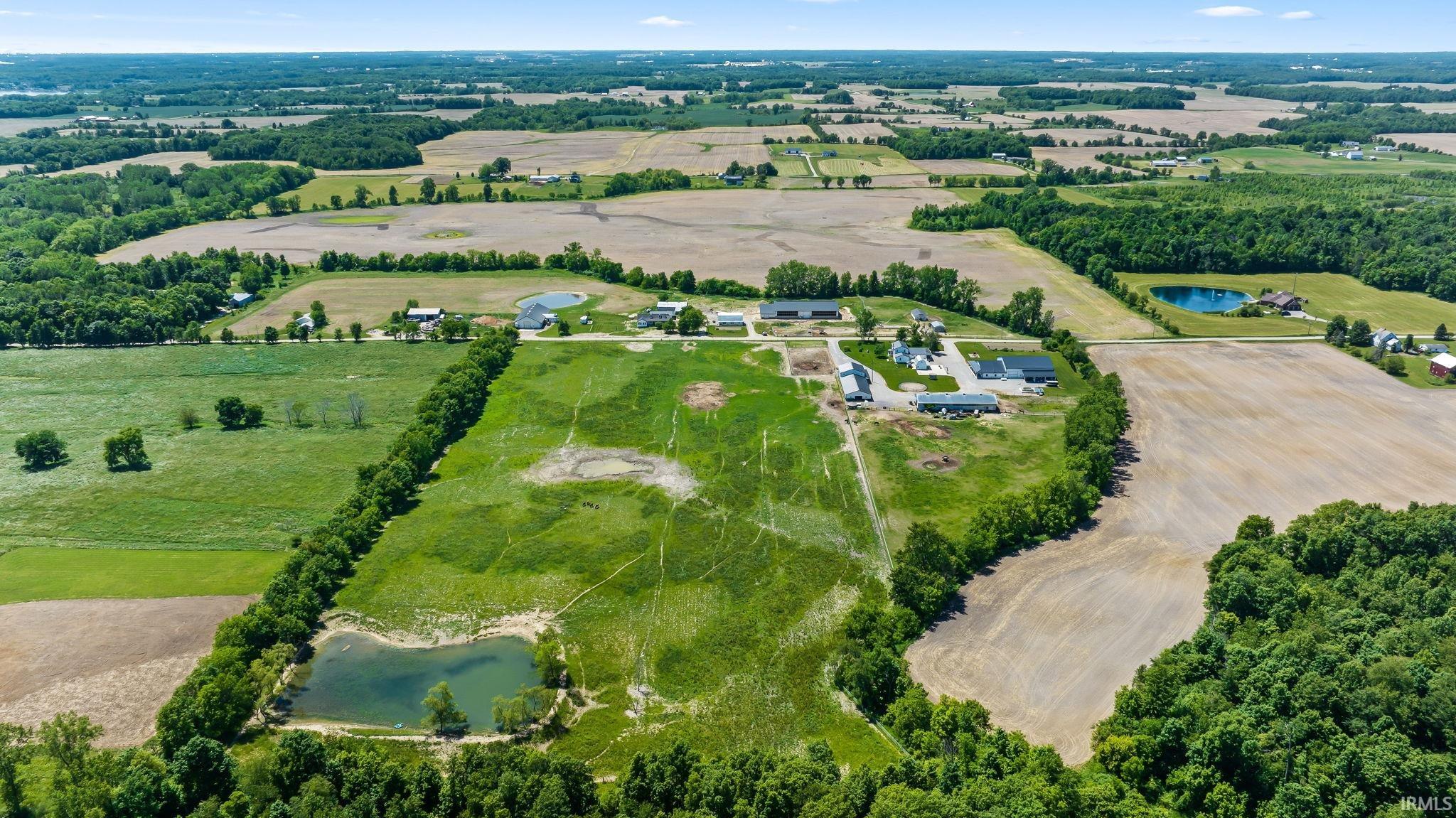 Expansive agricultural landscape featuring a private pond, multiple outbuildings, and a cleared building site