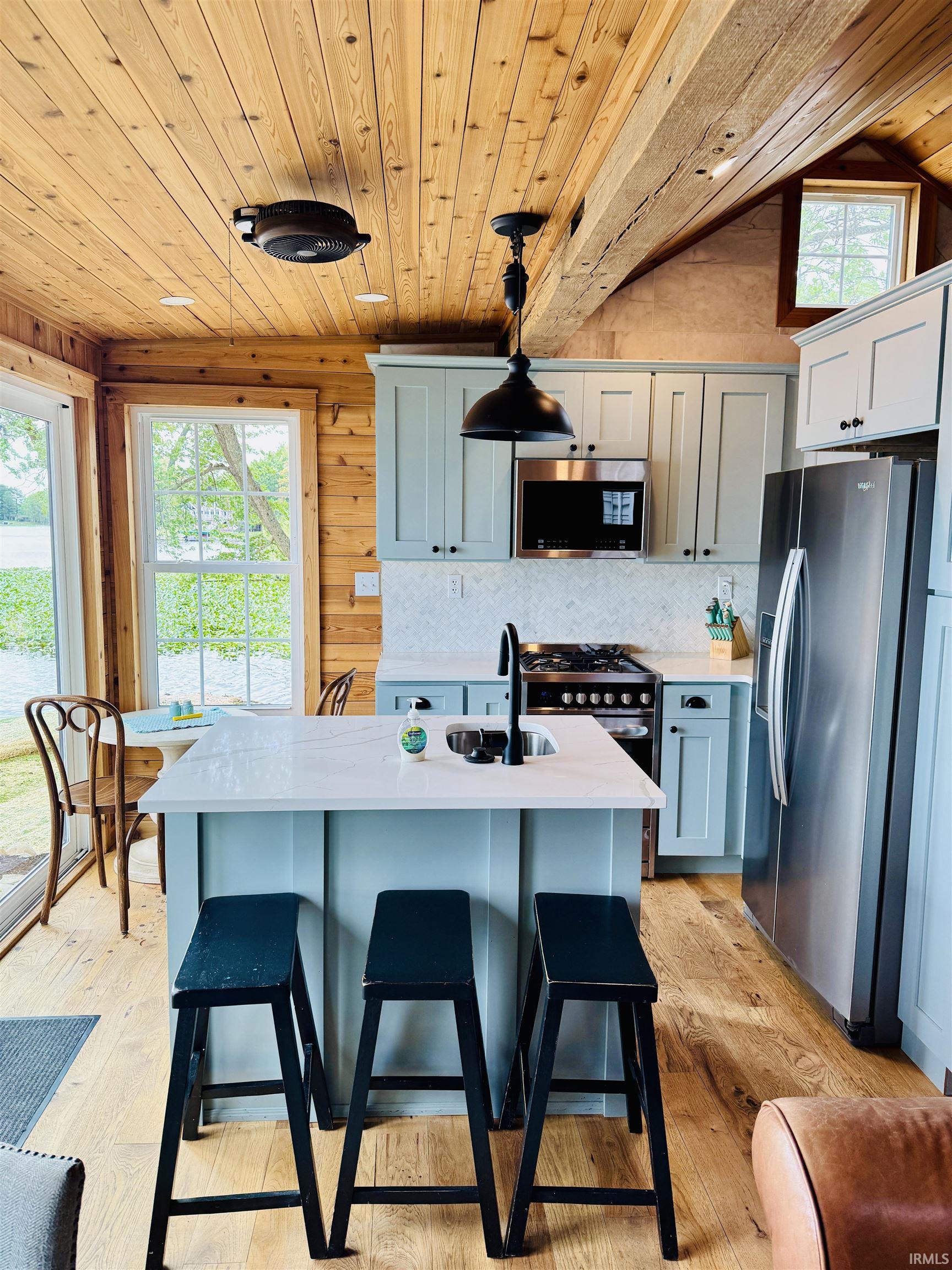 Modern kitchen featuring shaker-style cabinetry, a central island with integrated sink, stainless steel appliances, and wood-finish flooring