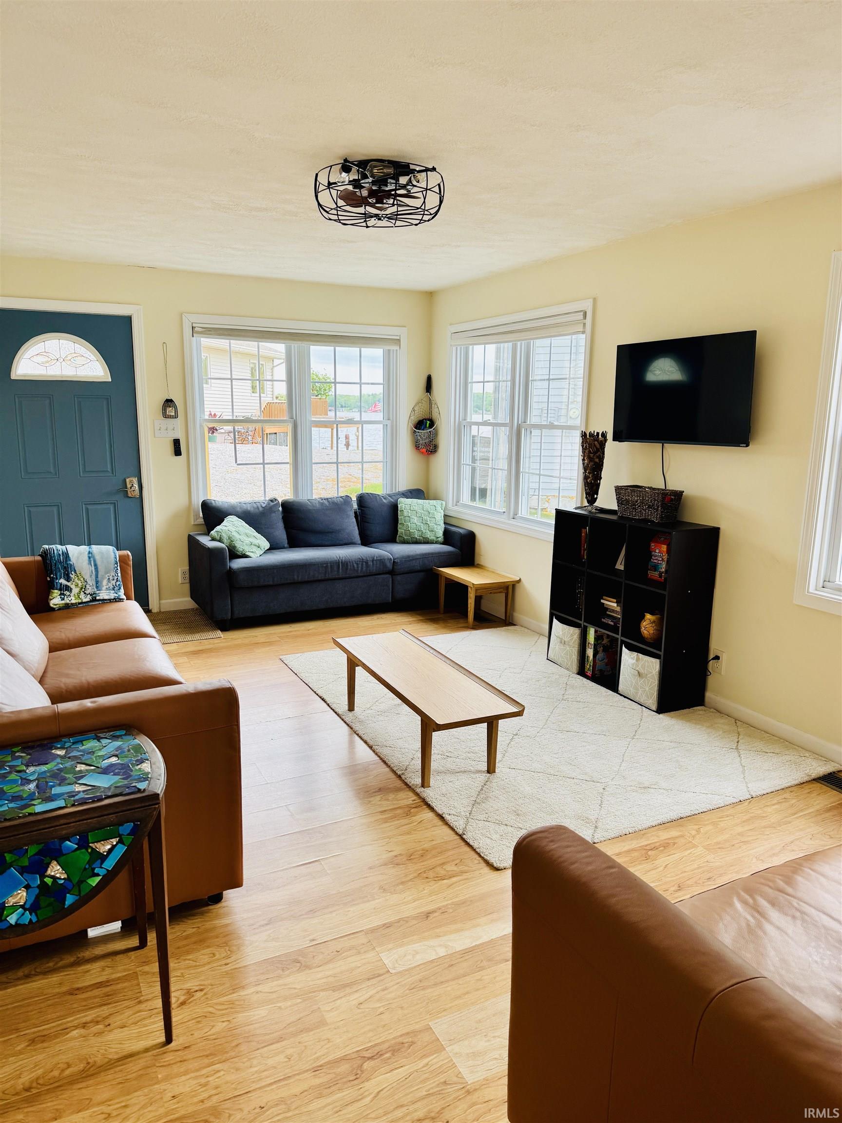 Bright living area featuring wood-finish flooring, a contemporary ceiling light fixture, and multiple windows allowing ample natural light