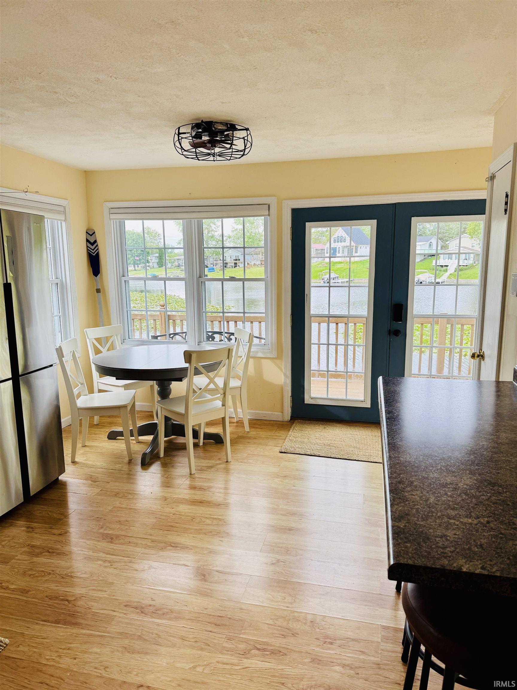 Dining area featuring wood-finish flooring, two large windows, and a glass-paneled door opening to a waterfront view