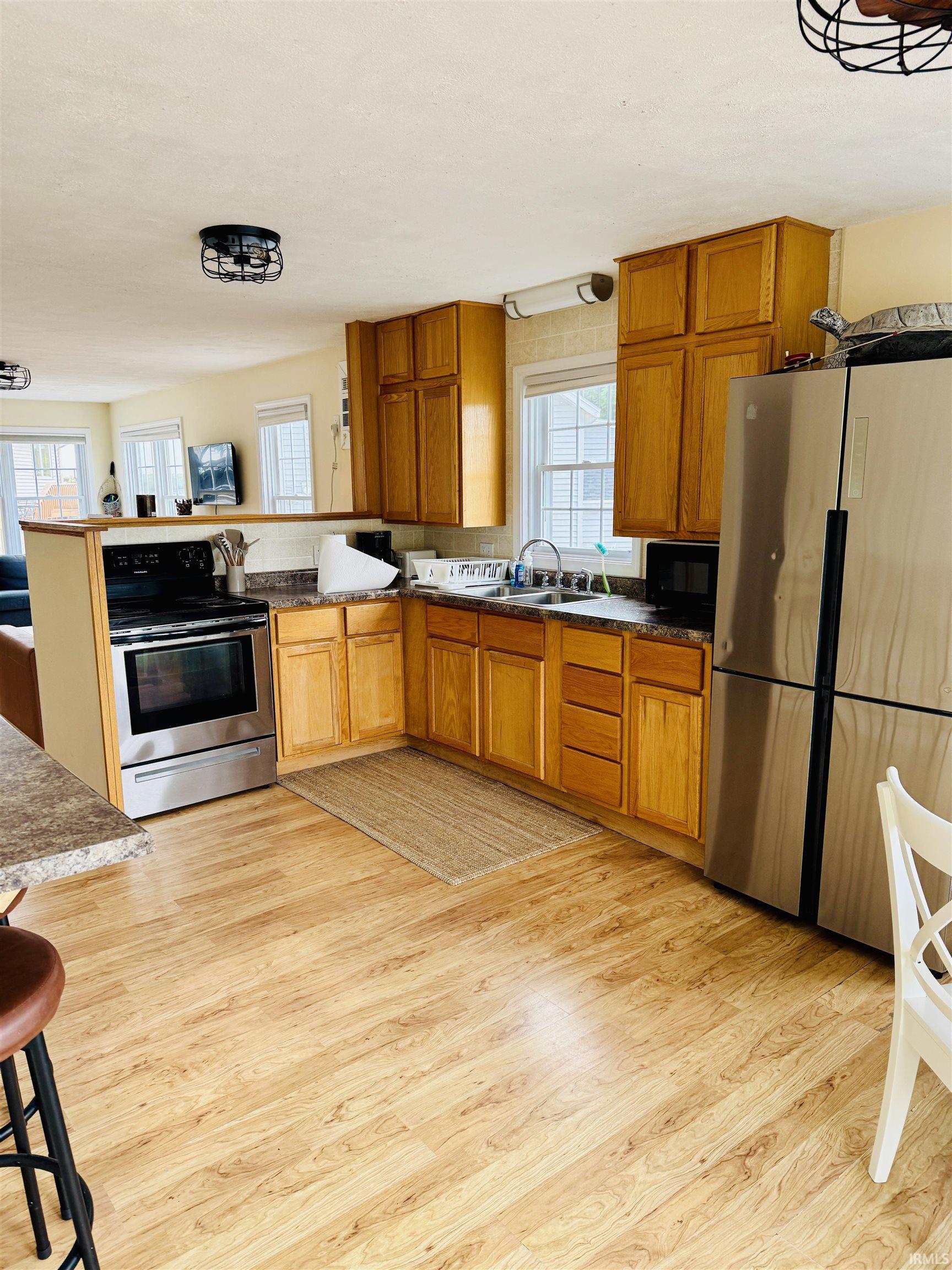 Kitchen featuring wood-finish flooring, light wood cabinetry, stainless steel appliances, and a double basin sink