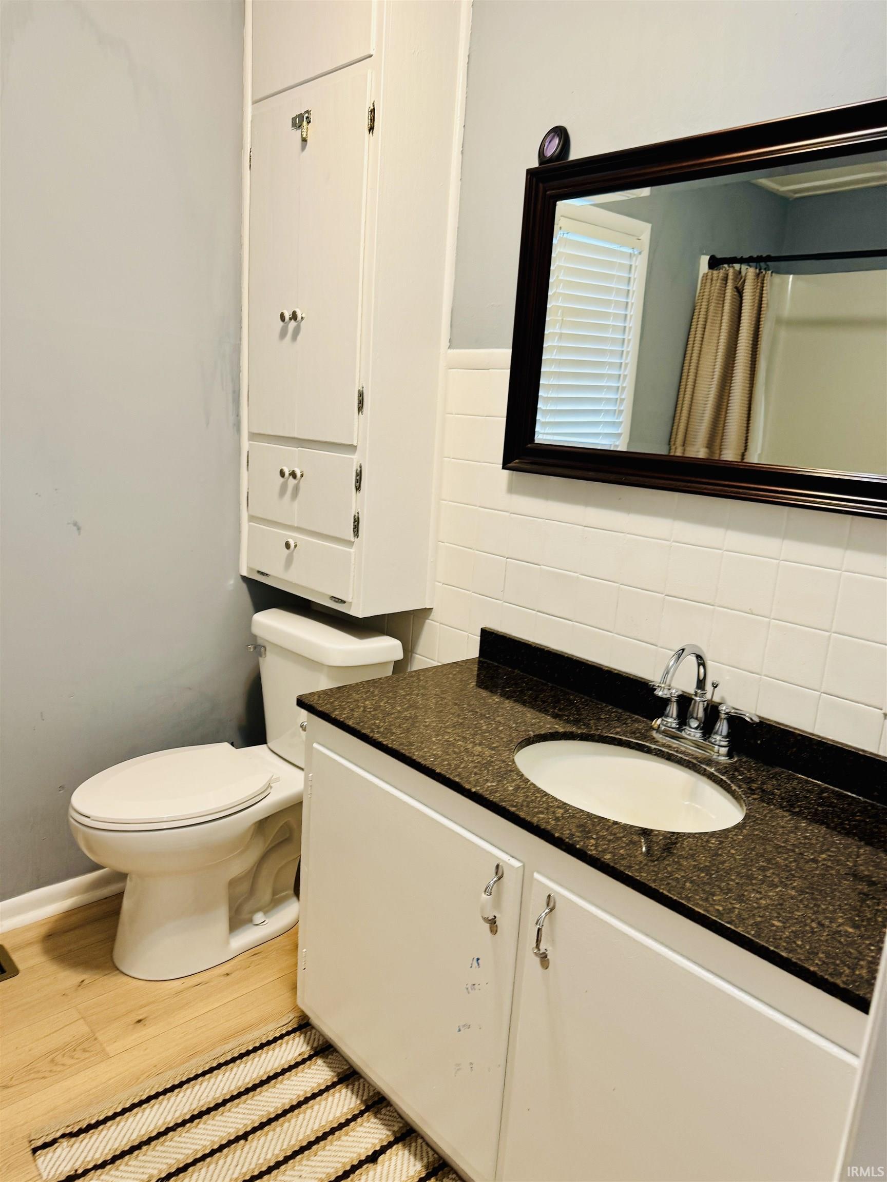 Bathroom featuring a built-in linen cabinet, white vanity with a dark speckled countertop, undermount sink, and wood-finish flooring